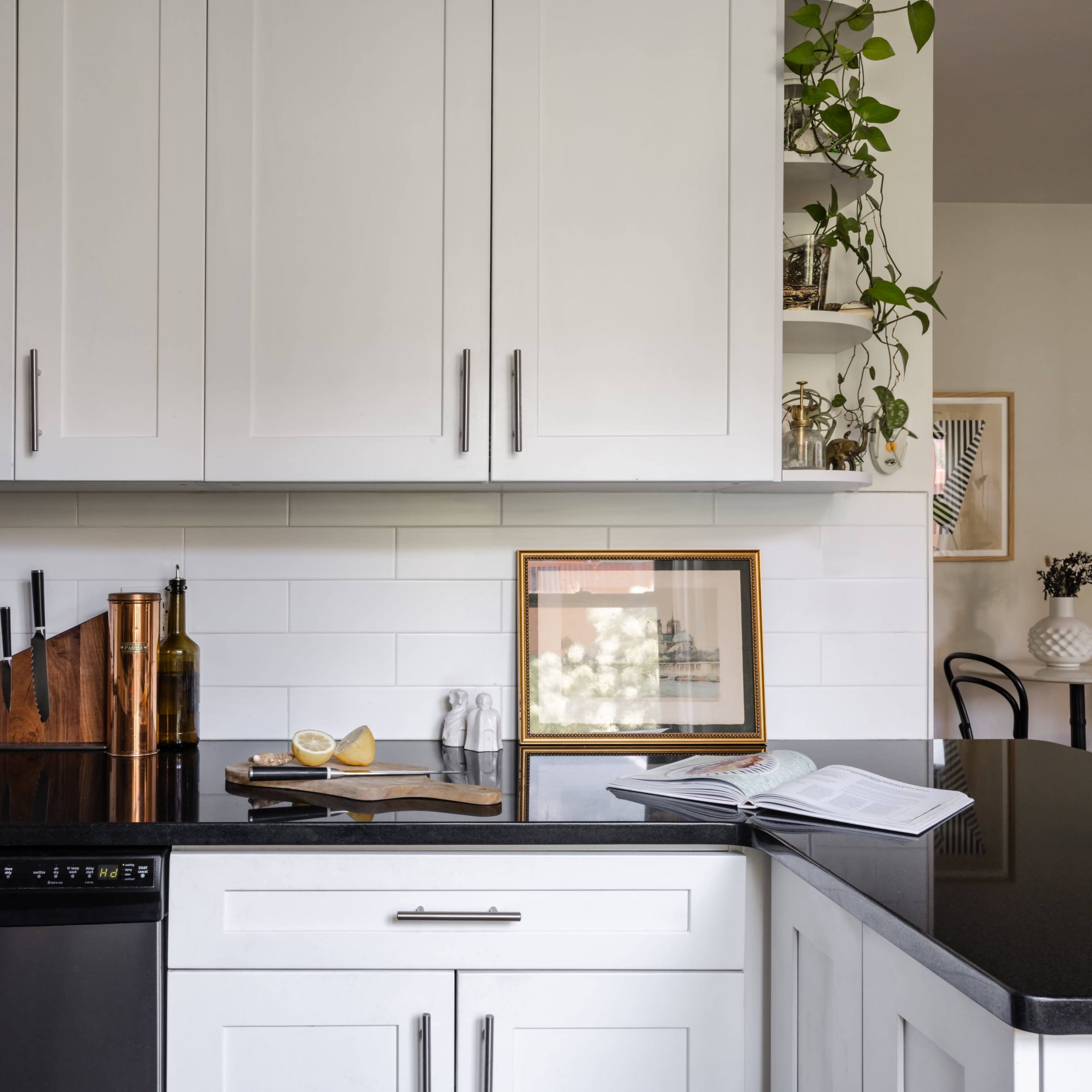 A modern kitchen features white cabinets, a black countertop, a stainless steel dishwasher, and decorative items on display.