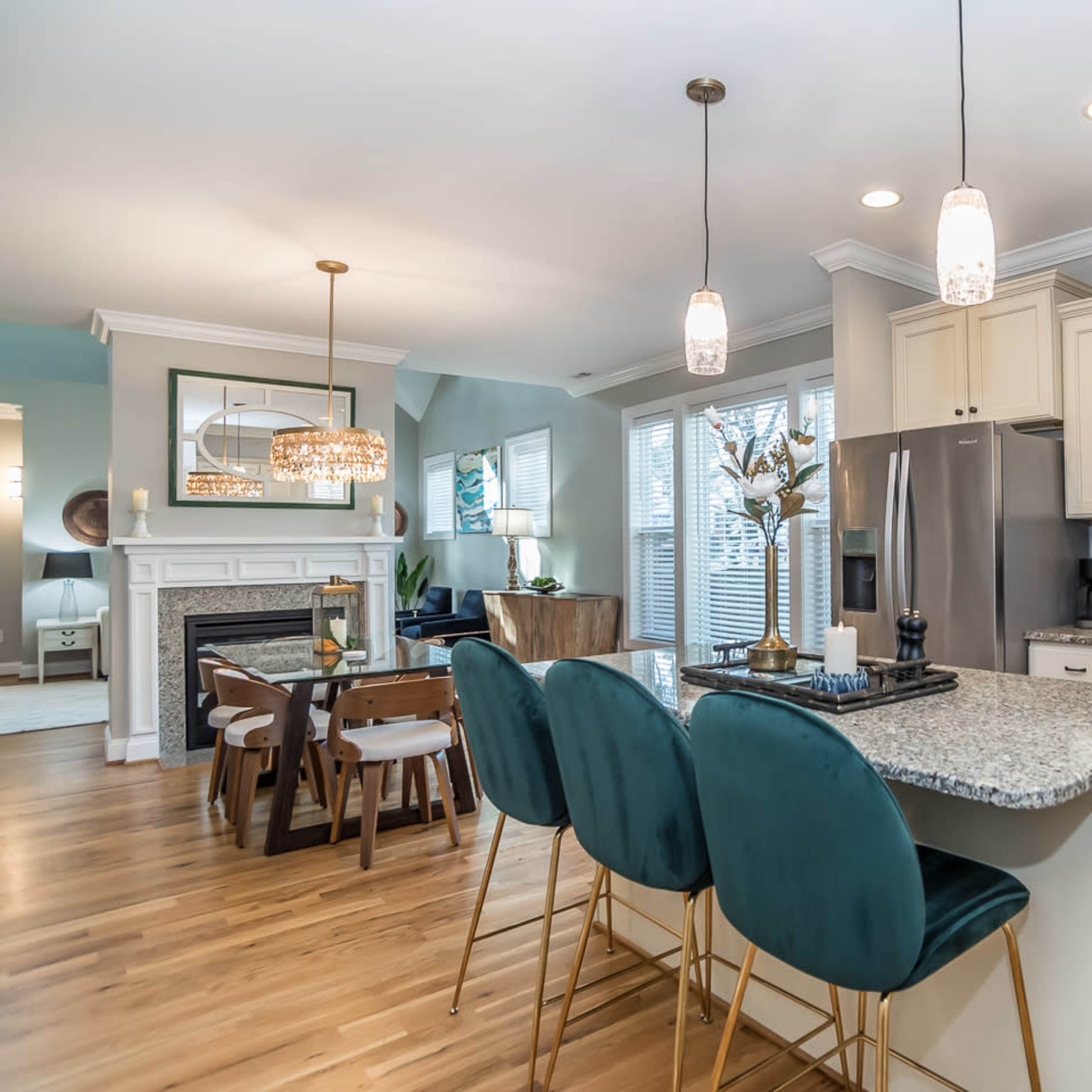 A modern kitchen features a large granite island with bar seating, stainless steel appliances, and an adjacent dining area, all illuminated by pendant lighting.