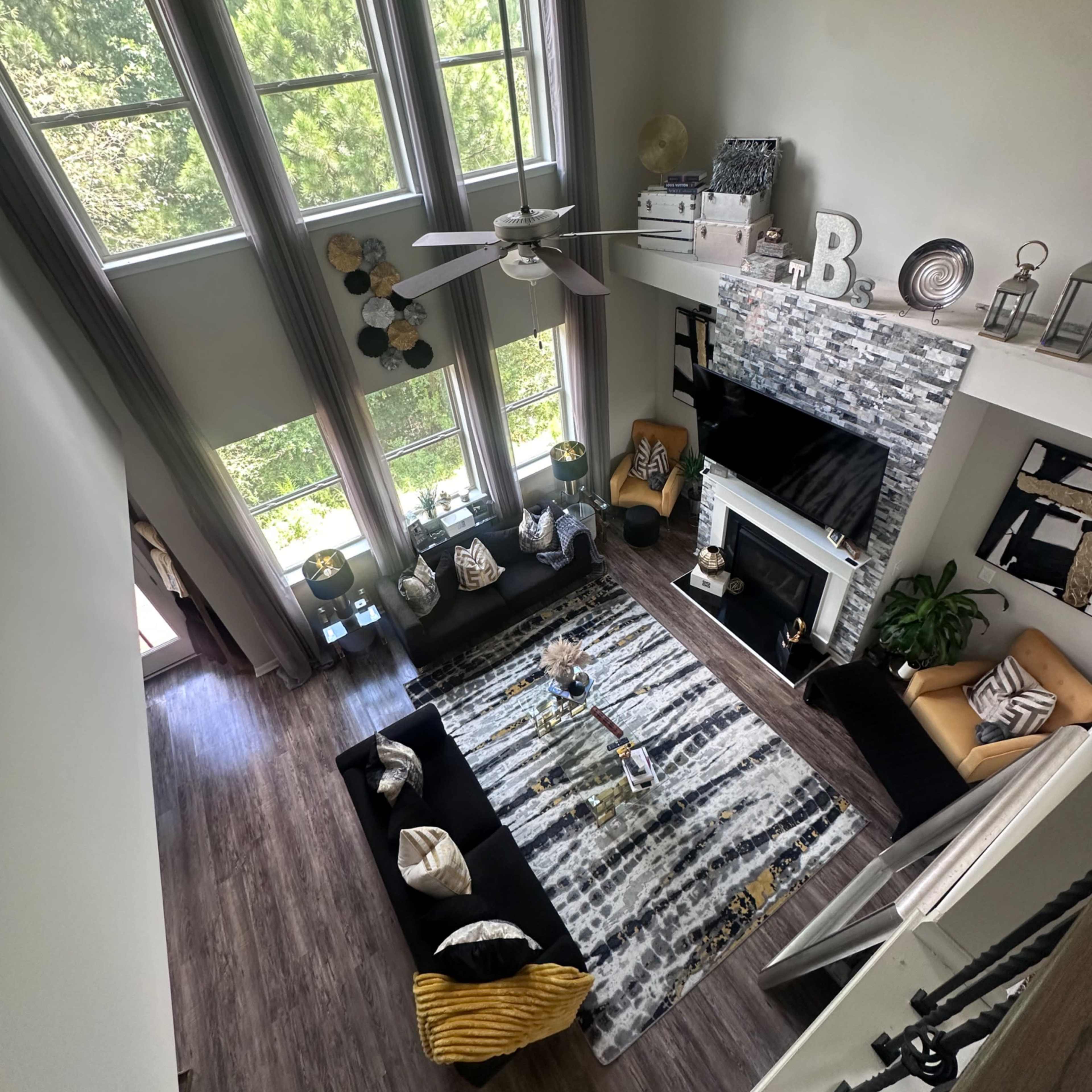 A spacious living room with tall windows, a patterned rug, and a fireplace, furnished with a mix of seating and decorative items.