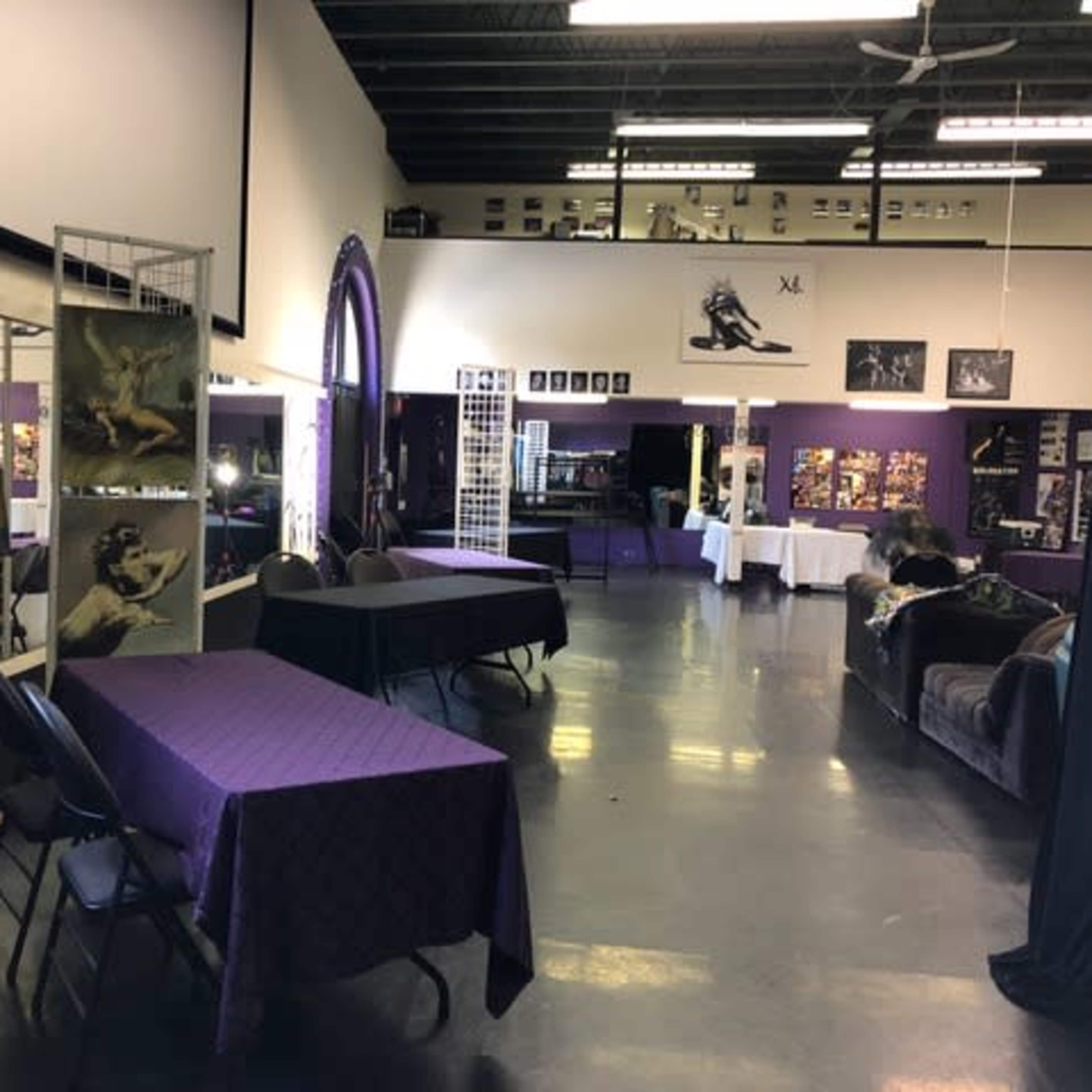A spacious interior with purple-draped tables, artwork on display, and various seating areas in a well-lit venue.