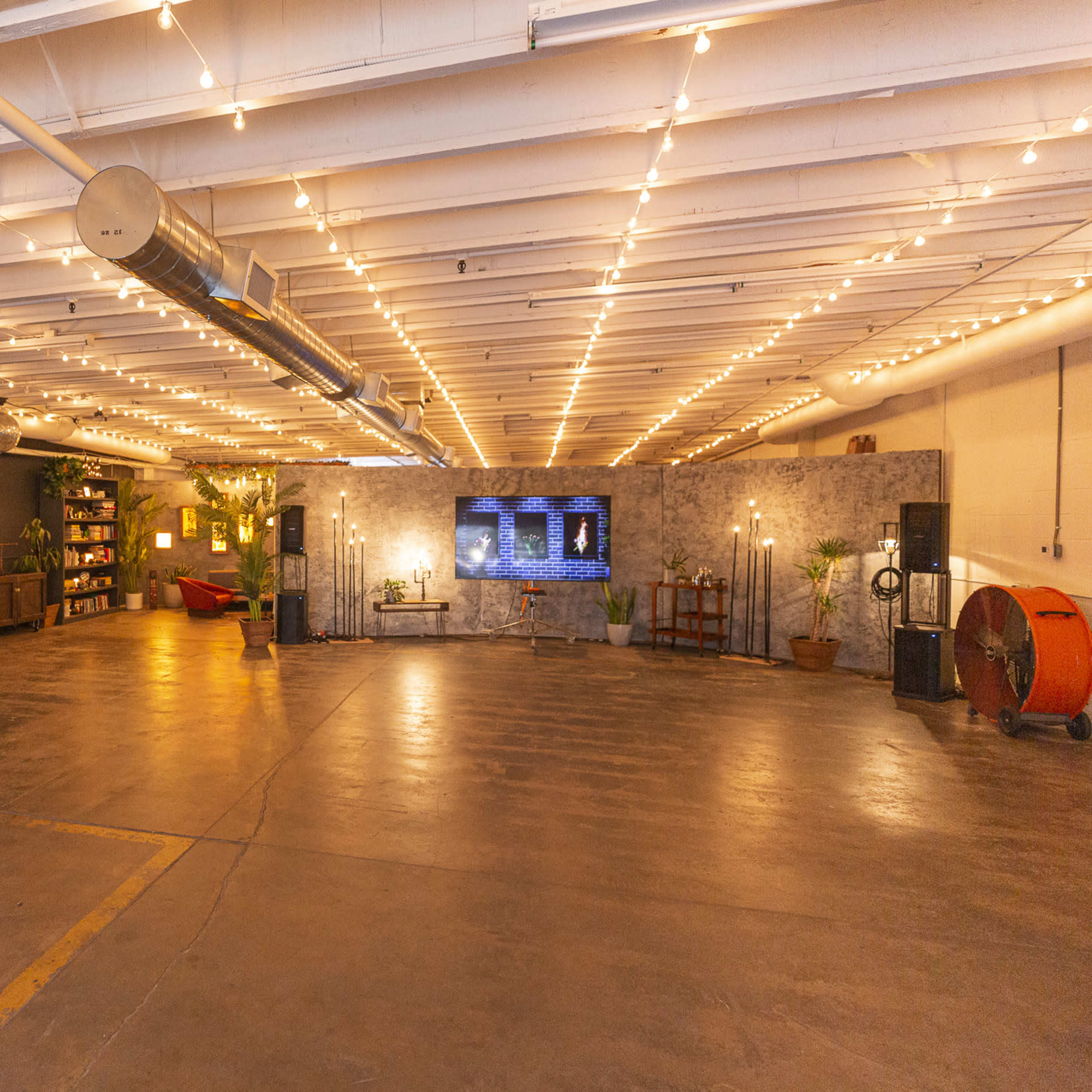 A spacious indoor area with string lights, a basketball hoop, seating, shelves, and a large screen on the wall.
