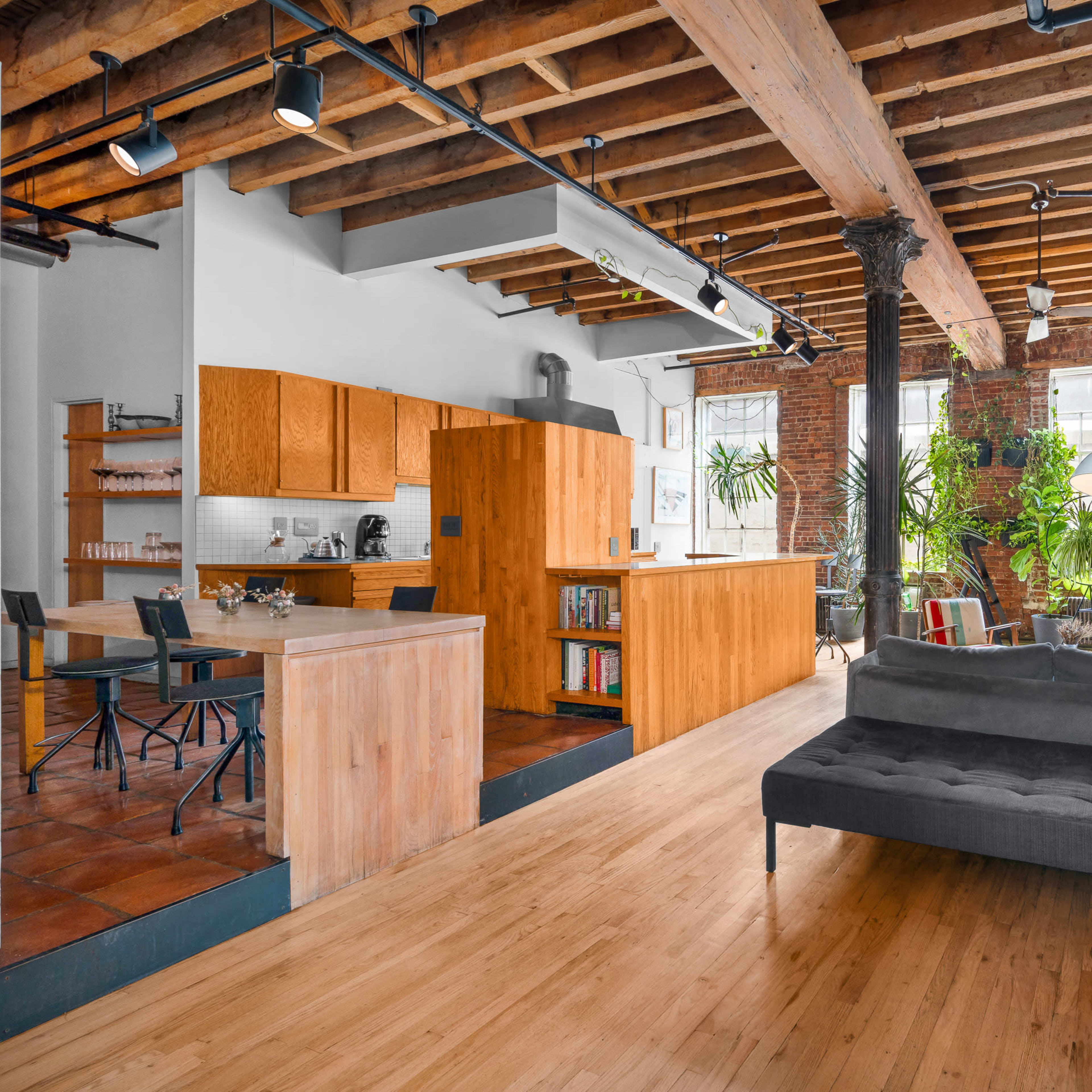 A spacious loft-style living area with wooden beams, an open kitchen, and abundant indoor plants.