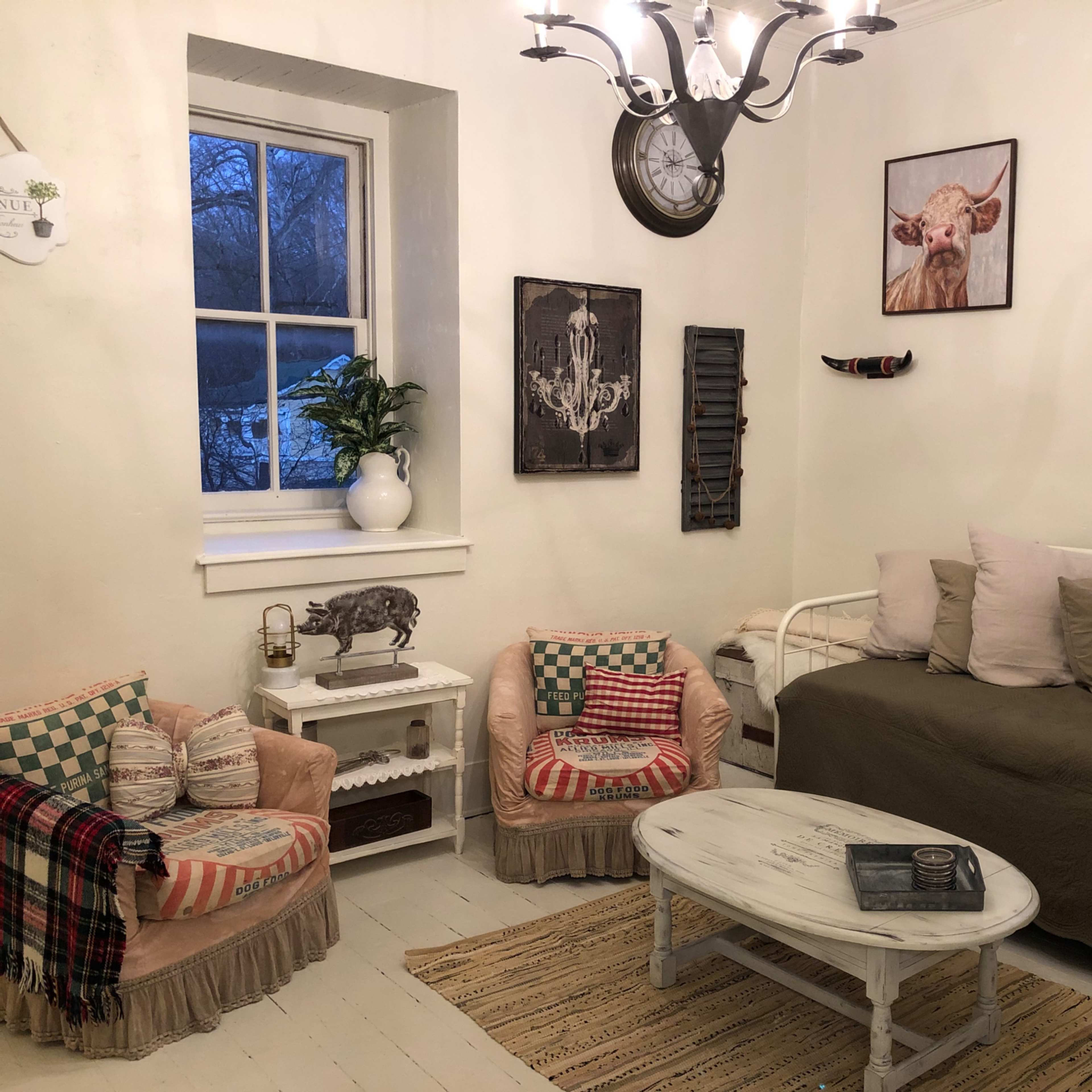 A cozy living room with a sofa, two armchairs, and a coffee table surrounded by light-colored walls and decorative wall art.