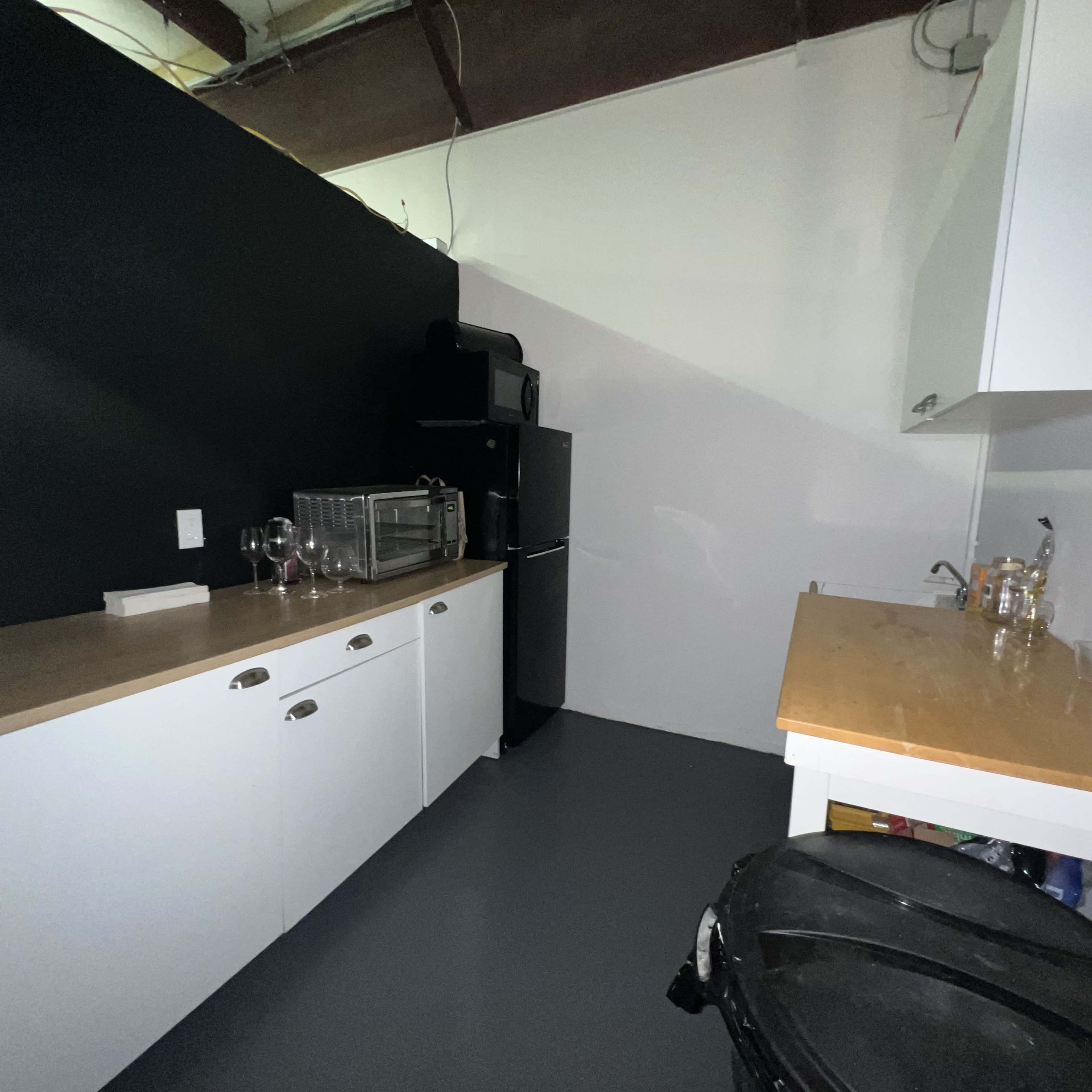 A kitchen area with a black wall, a refrigerator, two countertops, and a sink.