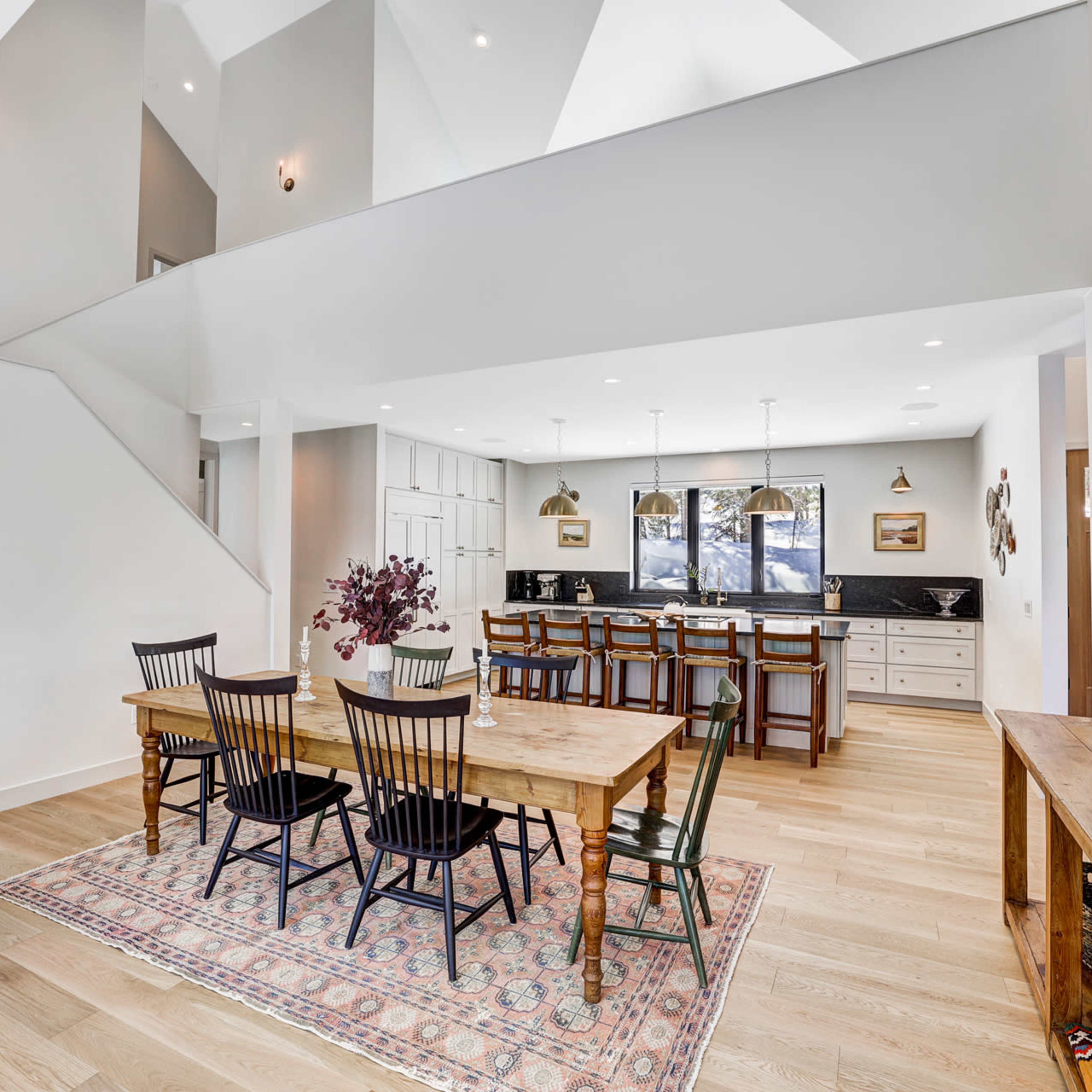 A spacious dining area with a wooden table and chairs, adjacent to a modern kitchen featuring bar seating and pendant lighting.