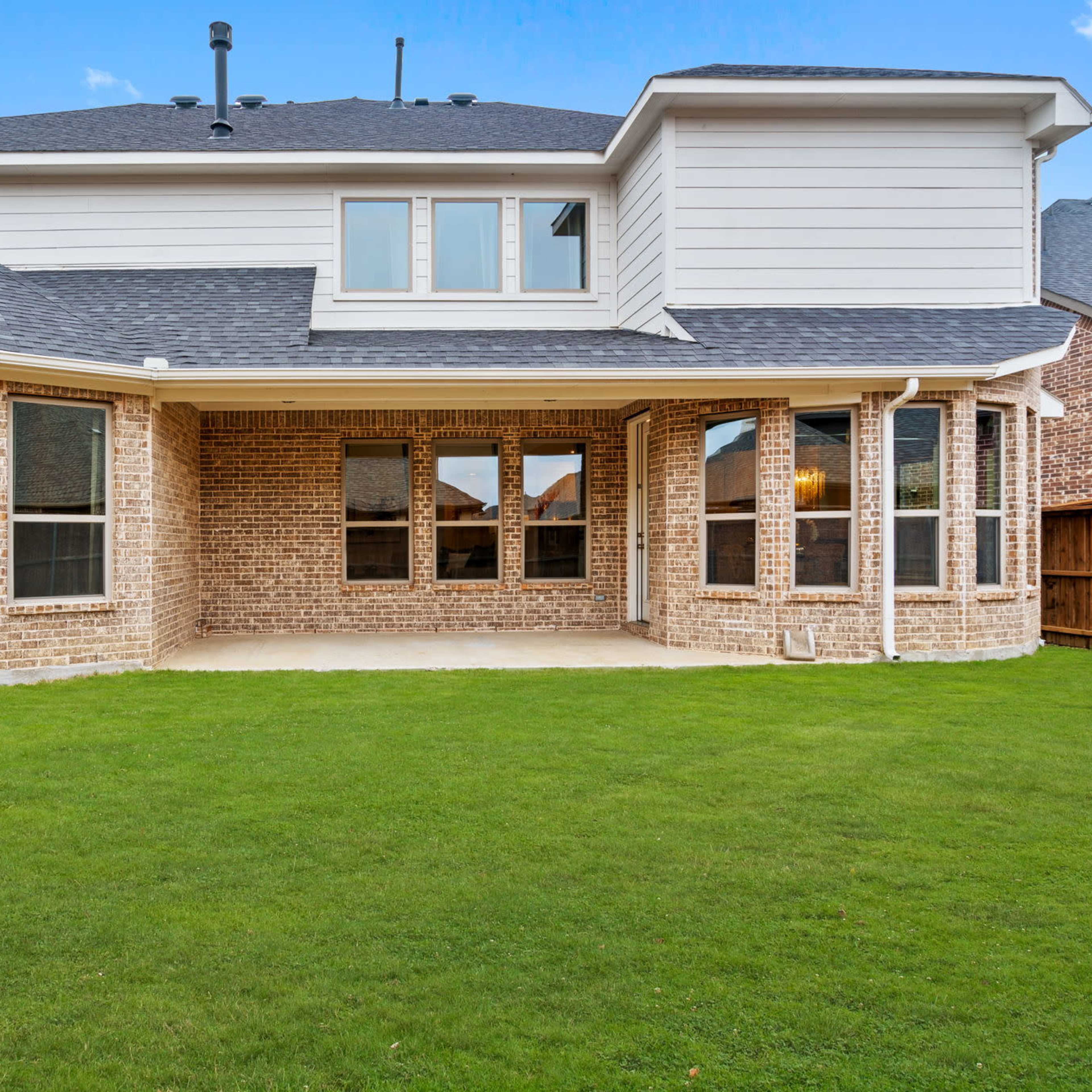 A backyard view of a two-story home with a brick exterior and large windows overlooking a grassy lawn.