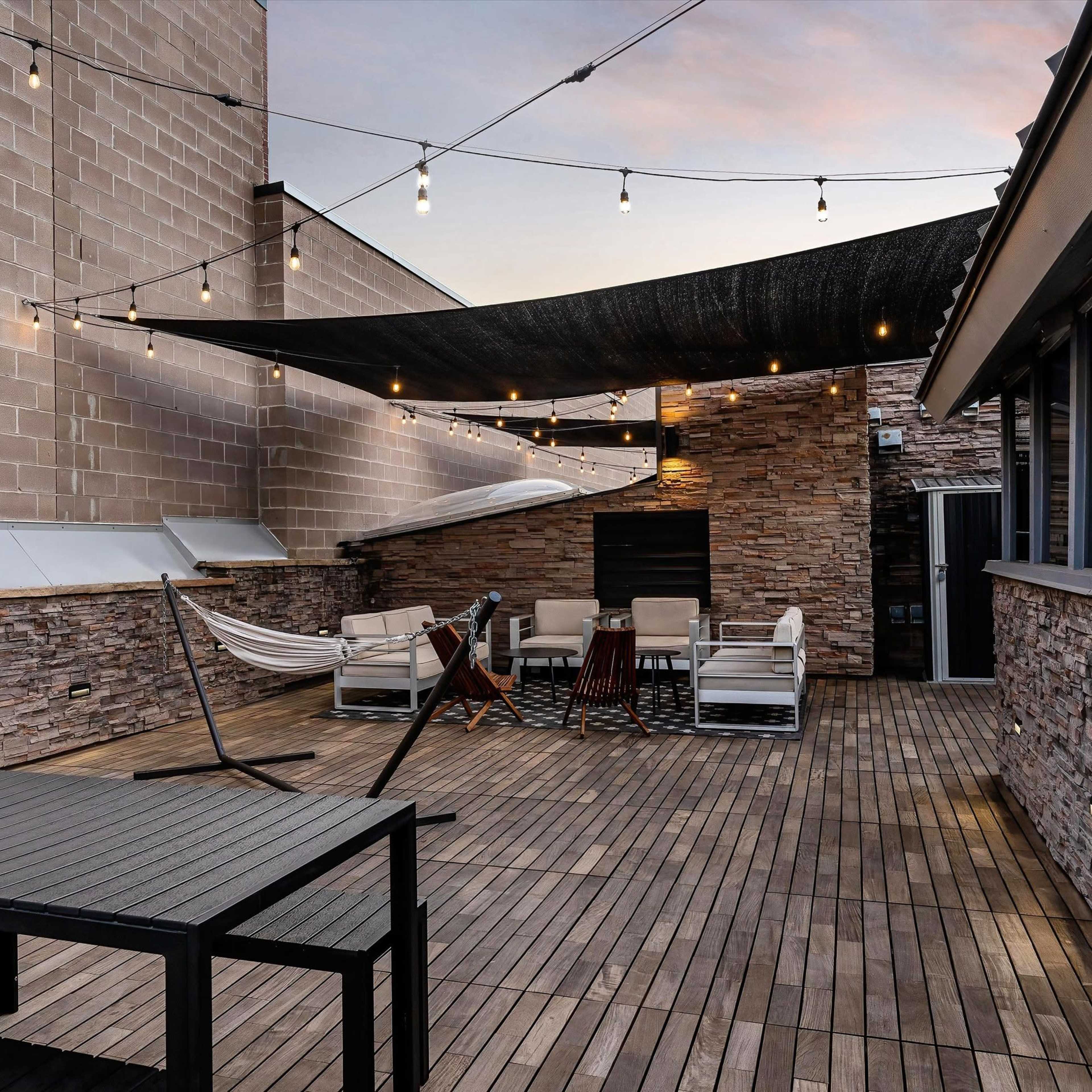 A spacious rooftop terrace features wooden flooring, lounge furniture, and string lights overhead.