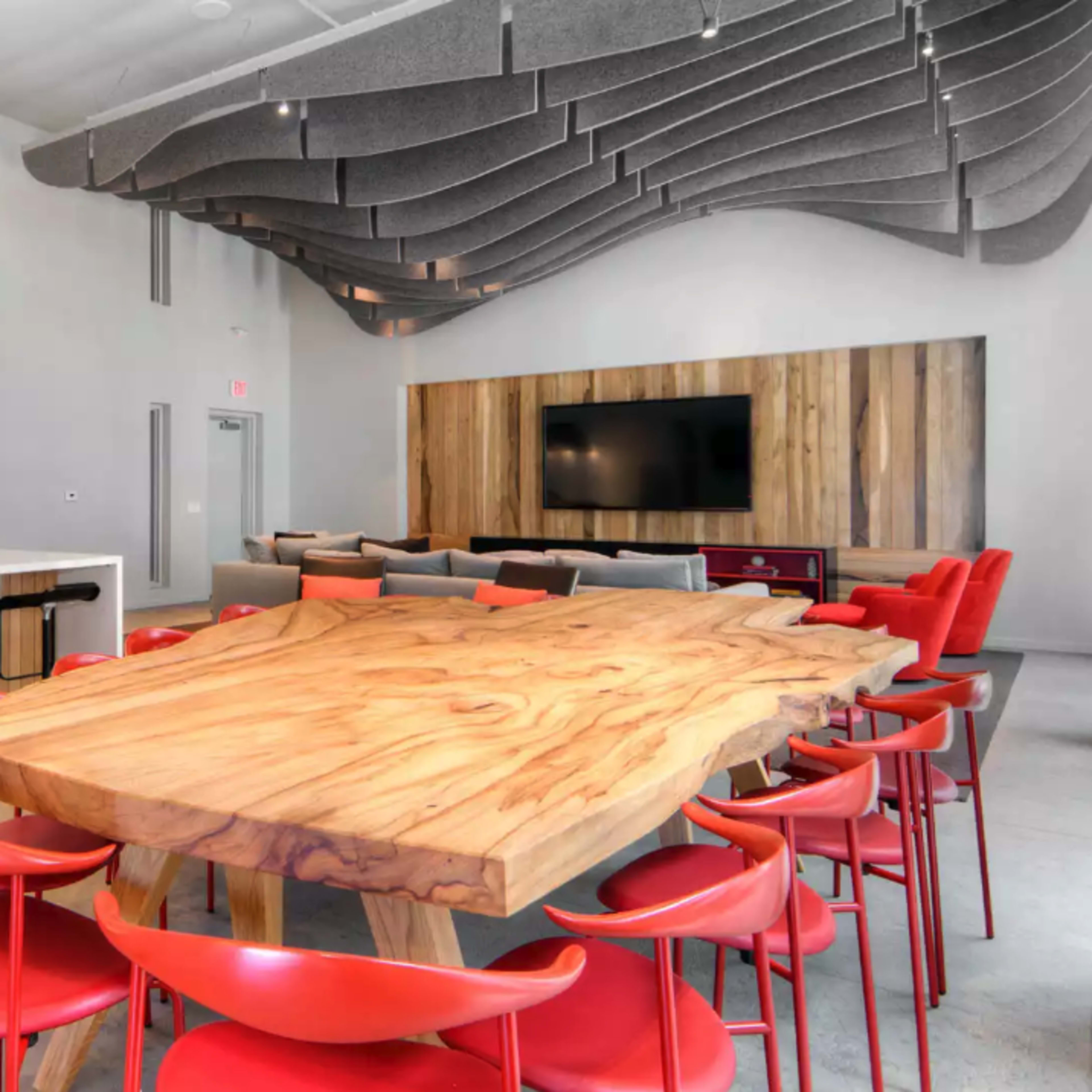 A modern kitchen and dining area featuring a large wooden table surrounded by red chairs, with a kitchen counter and sleek appliances in the background.