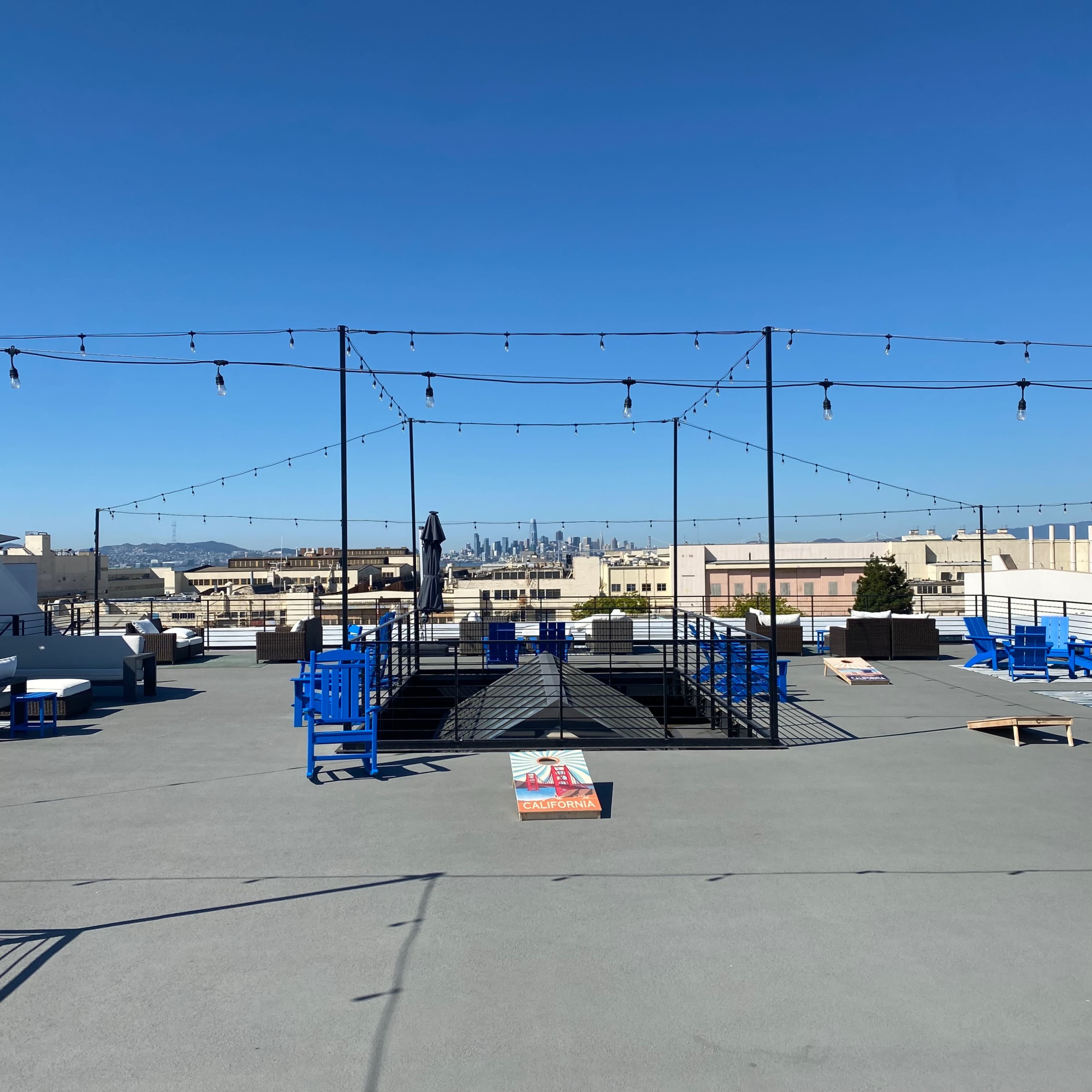 A spacious rooftop area features string lights overhead, blue and white furniture, and a distant view of city skyscrapers.
