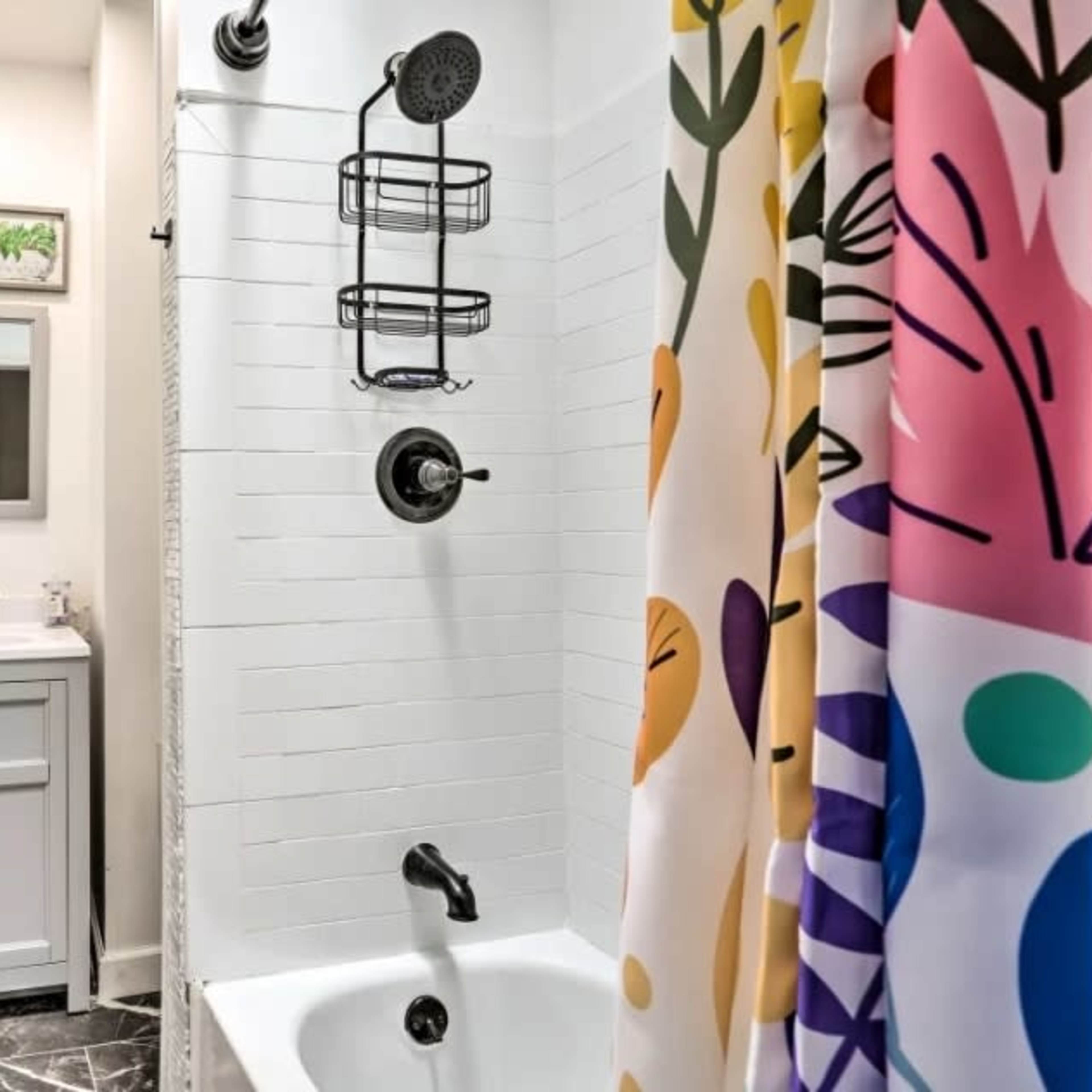 A bathroom featuring a shower with a colorful curtain, a wall-mounted shelving unit, and a vanity with a mirror.