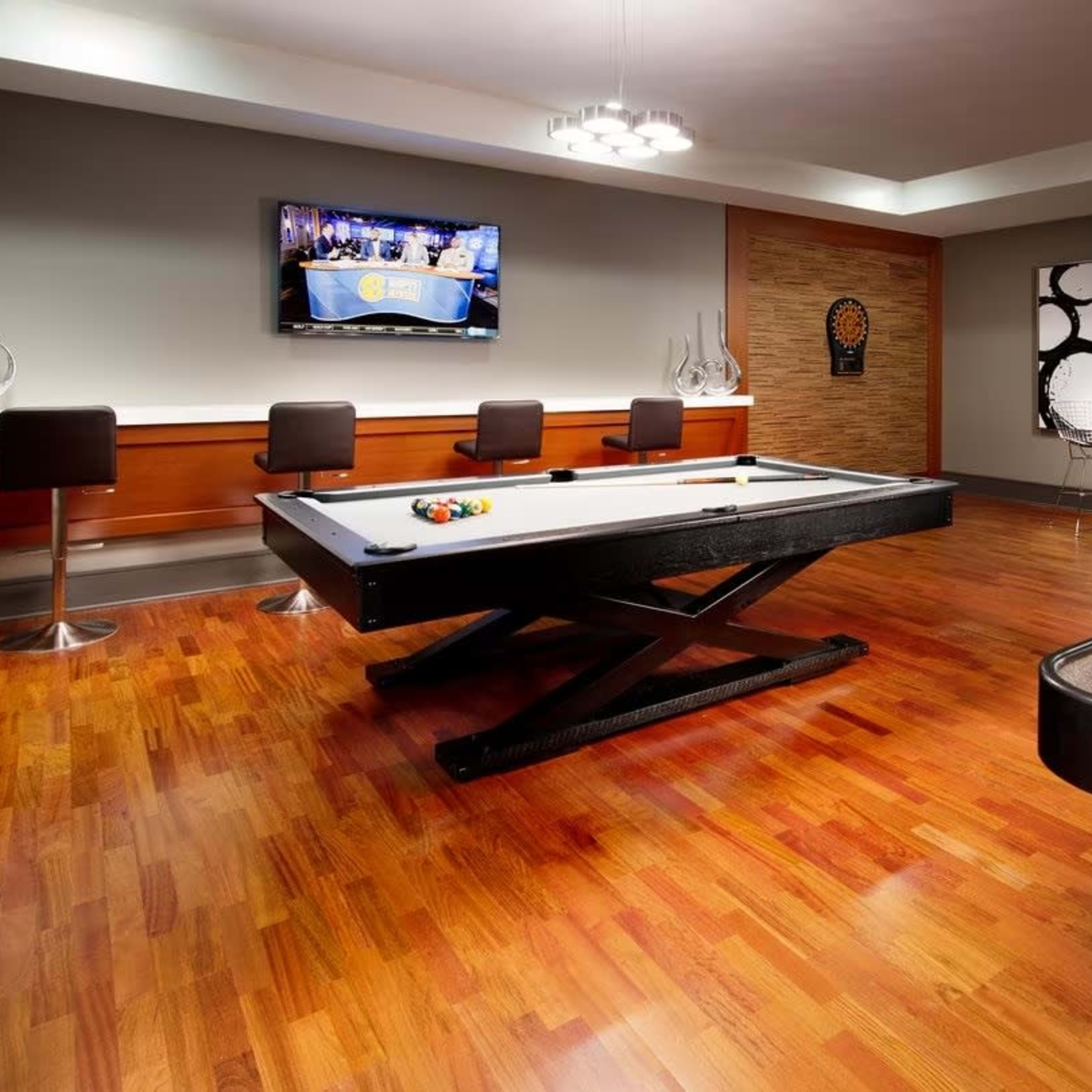 A recreational room with a pool table, a shuffleboard table, bar stools, and a television mounted on the wall.