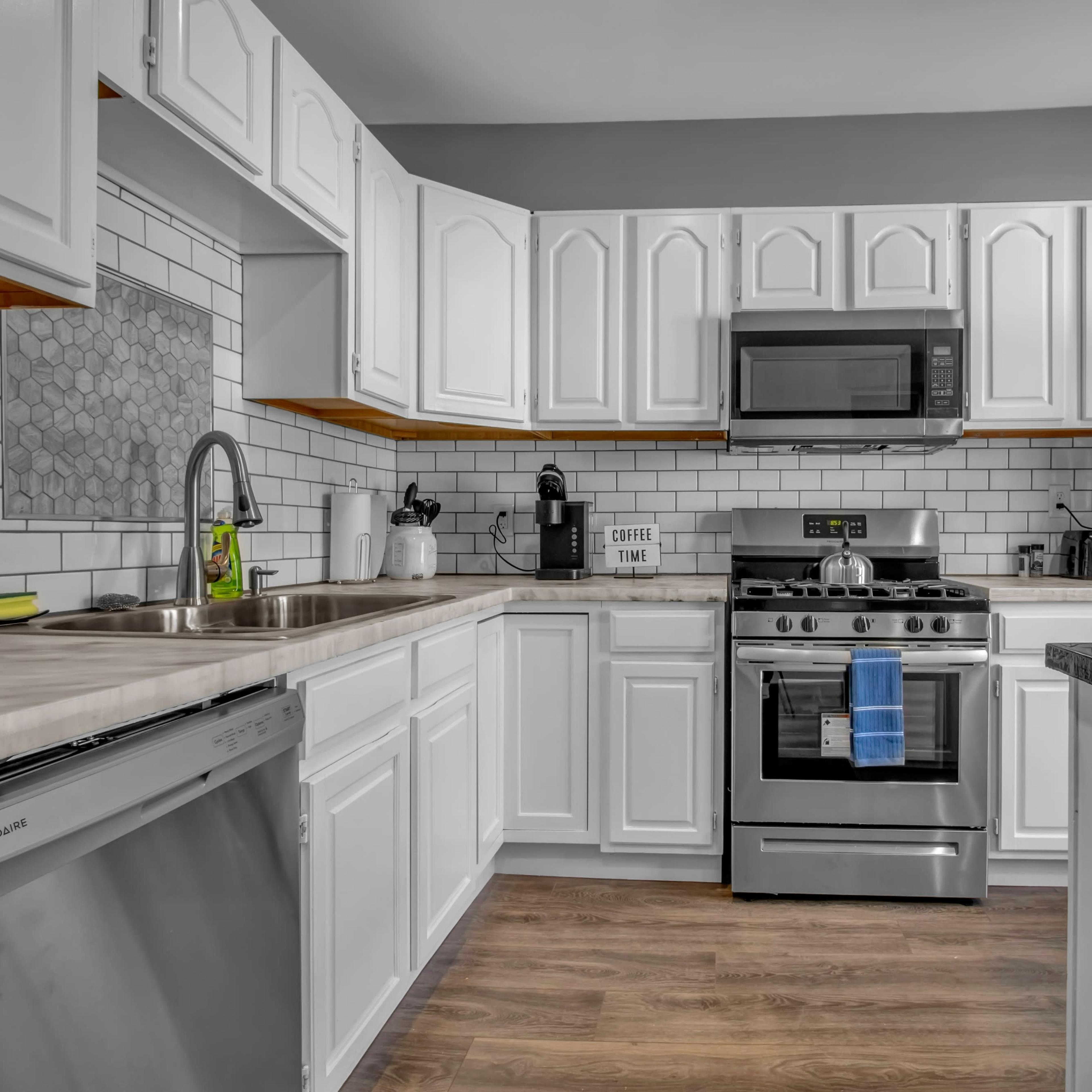 A modern kitchen features white cabinetry, stainless steel appliances, and a beige countertop with a sink and dishwasher.