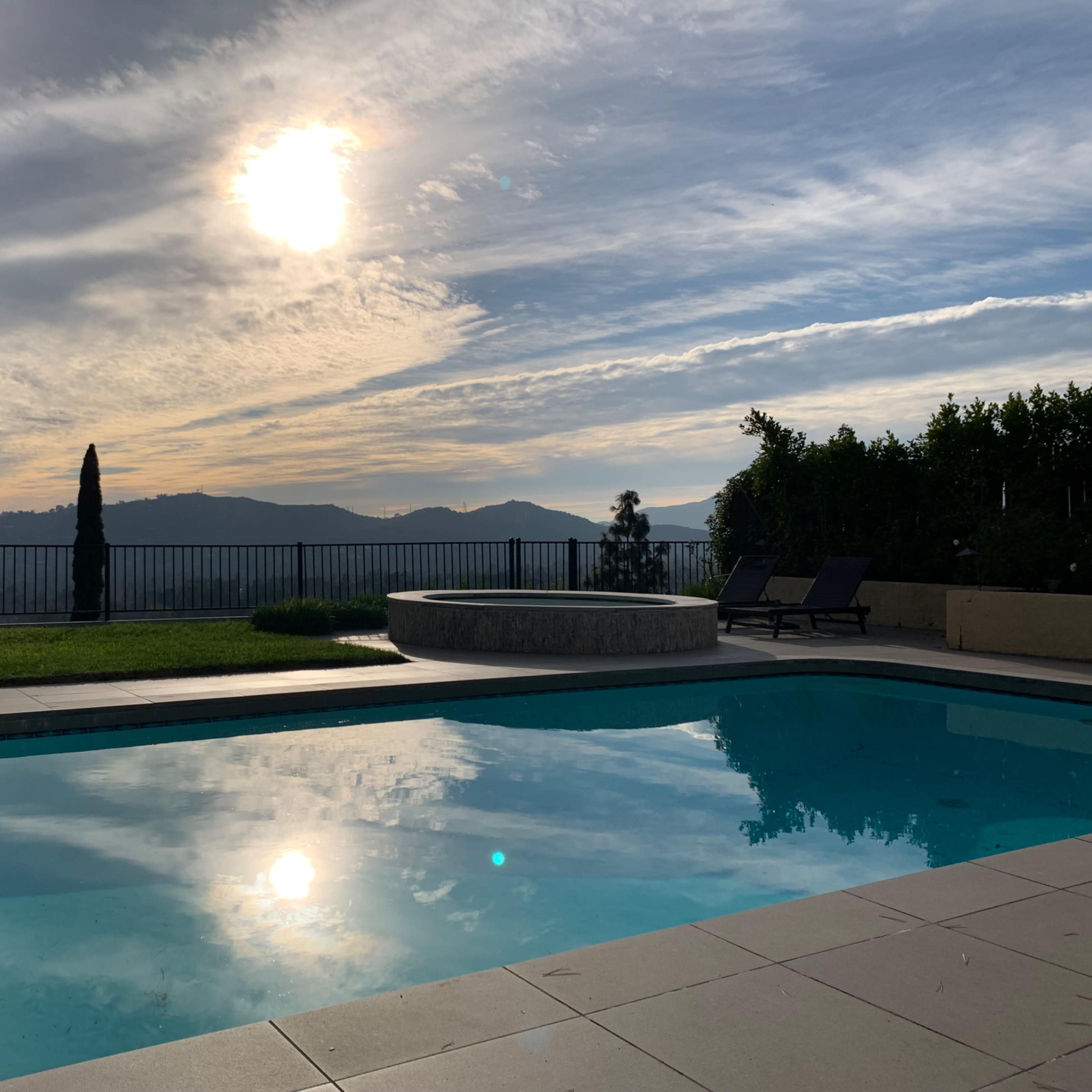 A serene pool reflecting the sun and surrounding hills under a partly cloudy sky.
