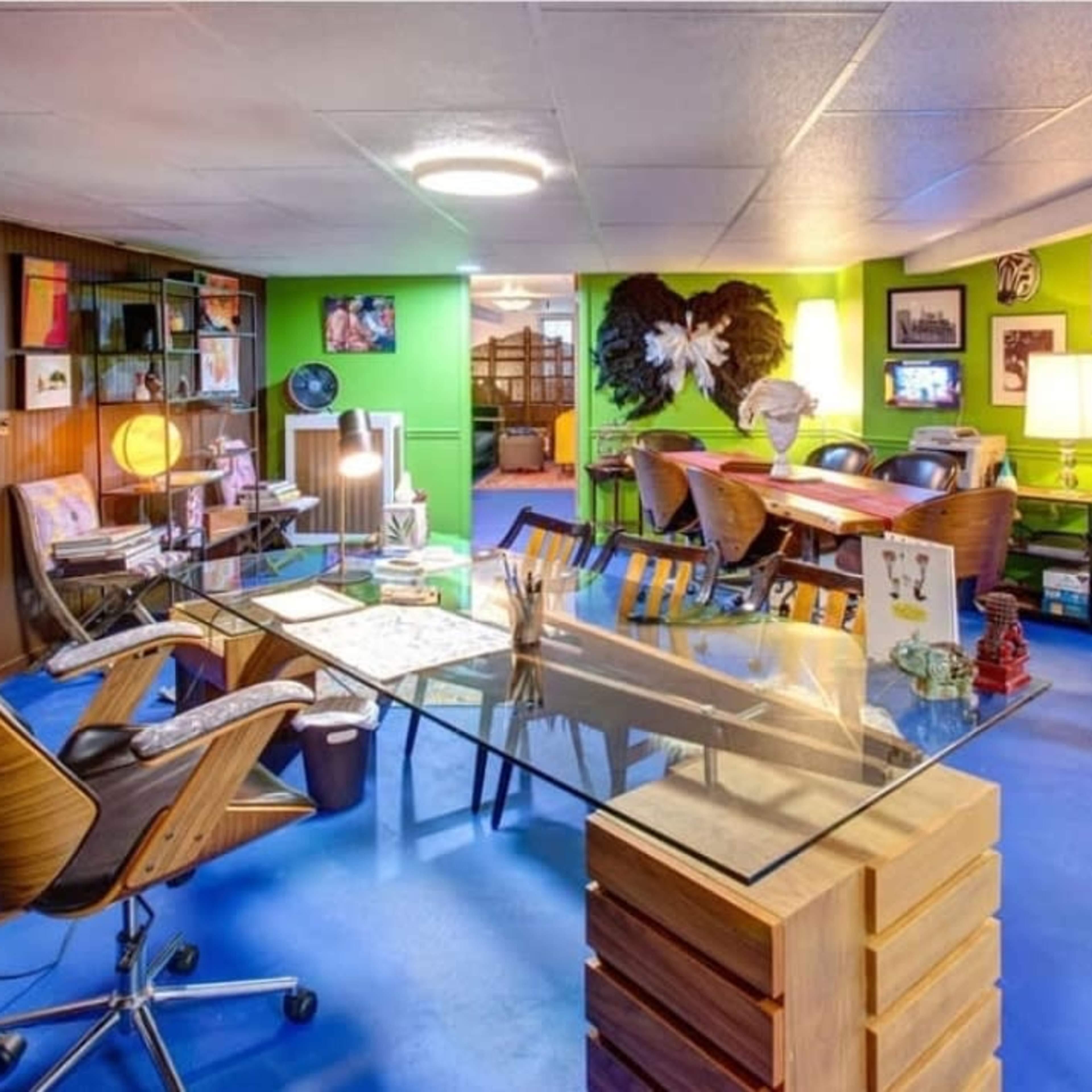 A vibrant basement space featuring a glass desk with wooden chairs, colorful walls, and various tables and seating areas.