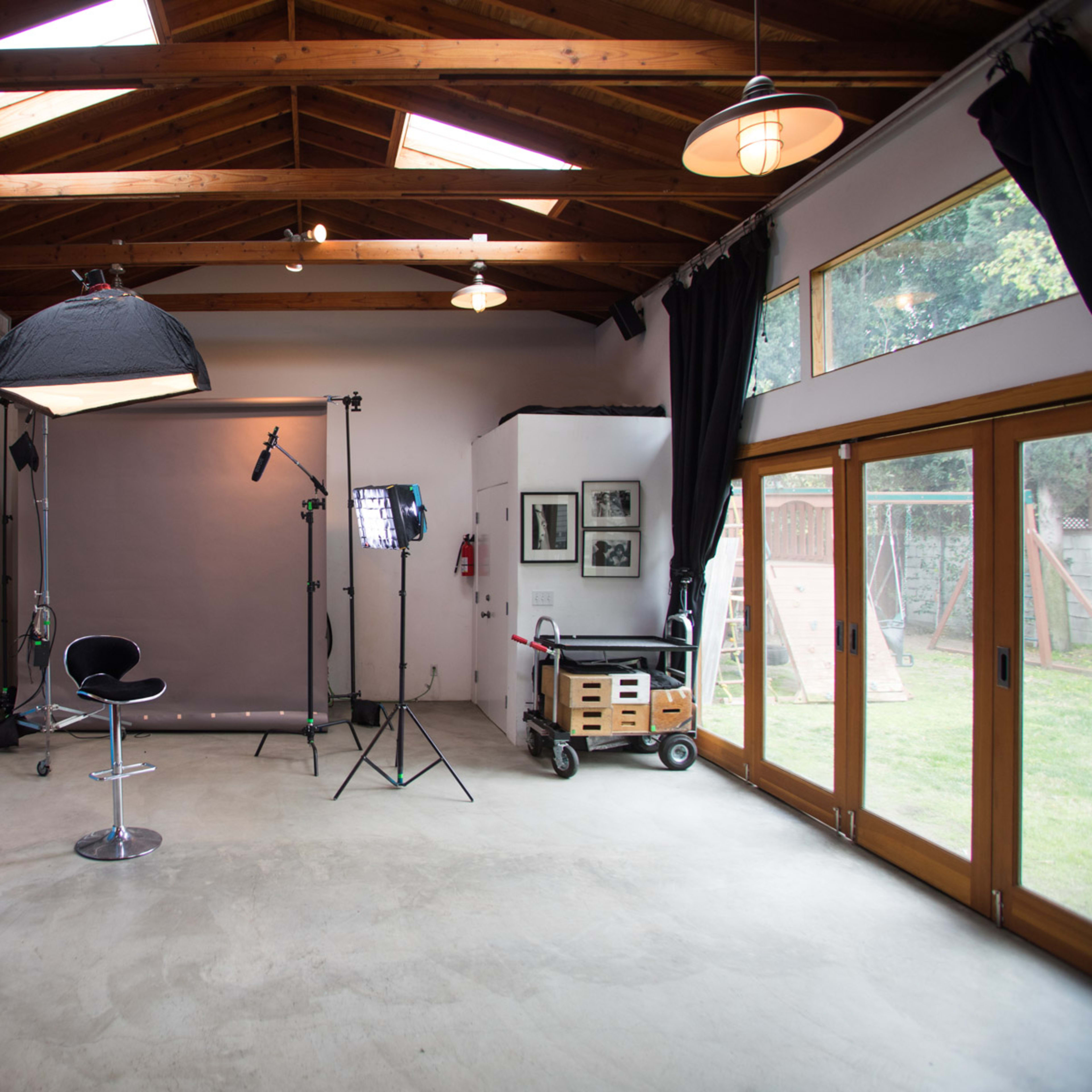 A spacious photography studio featuring a blue backdrop, a gray backdrop, lighting equipment, and large windows that provide natural light.