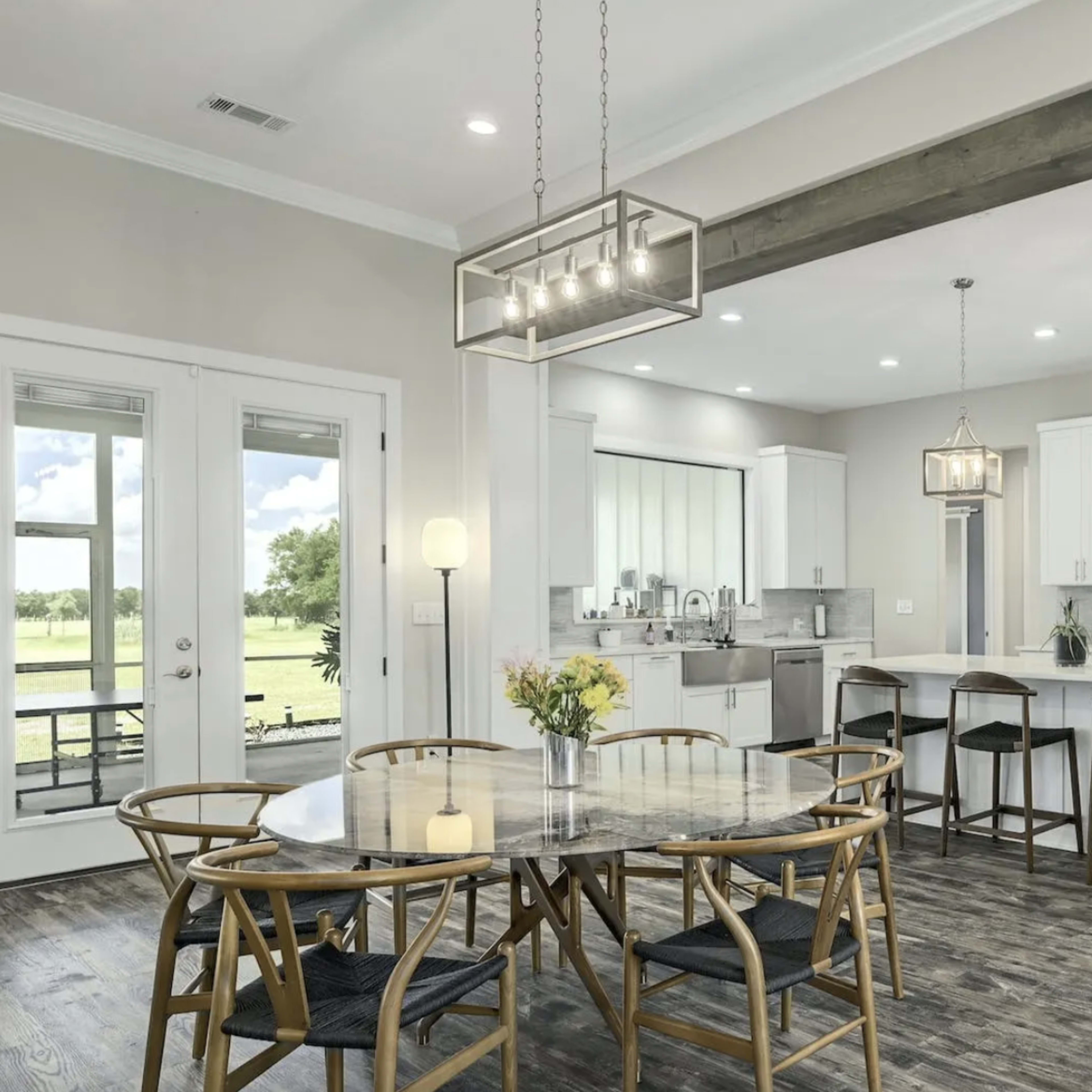 A modern kitchen and dining area with a round table, wooden floors, and large windows that allow natural light to fill the space.