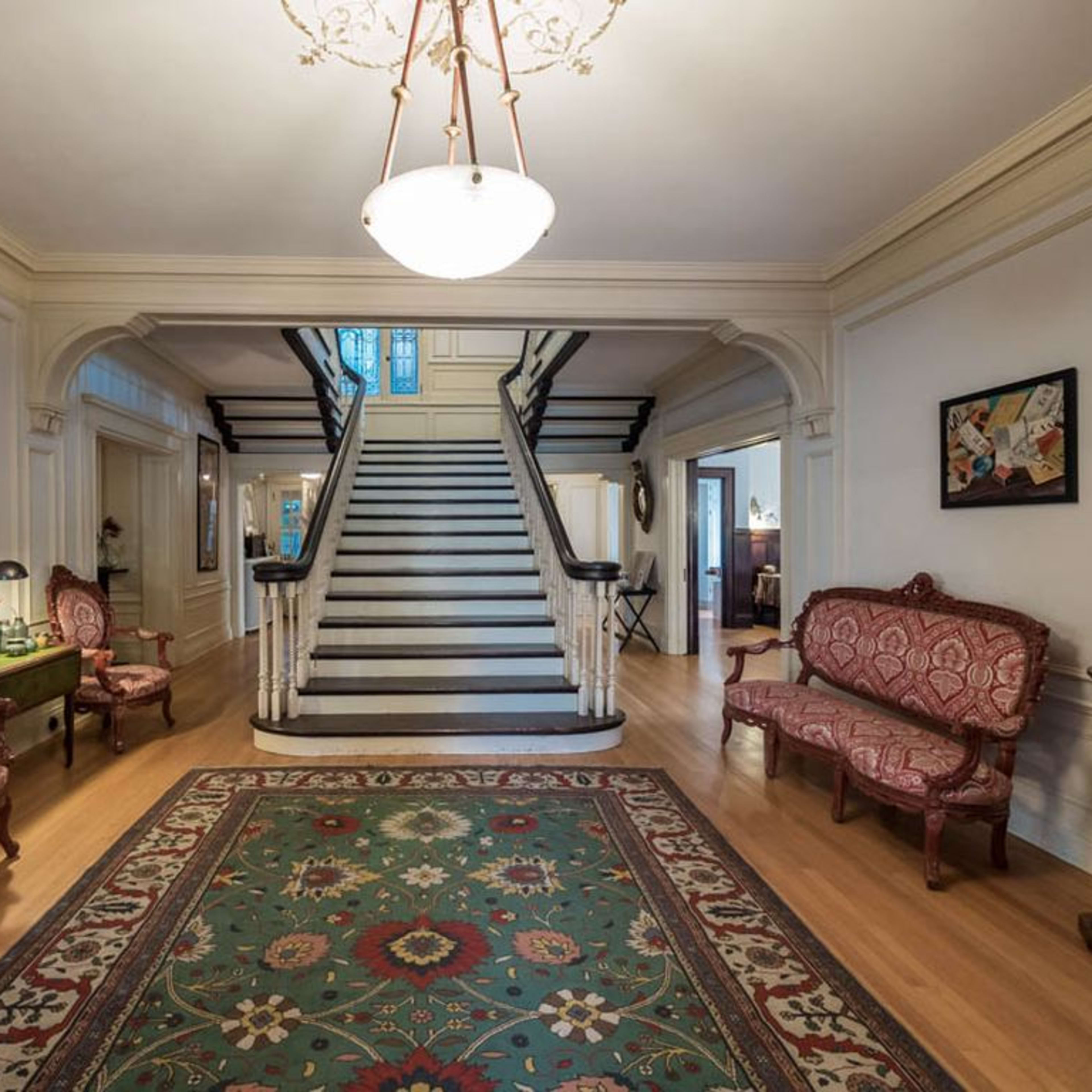 A large foyer featuring a staircase, two ornate chairs, and a decorative rug on a wooden floor.