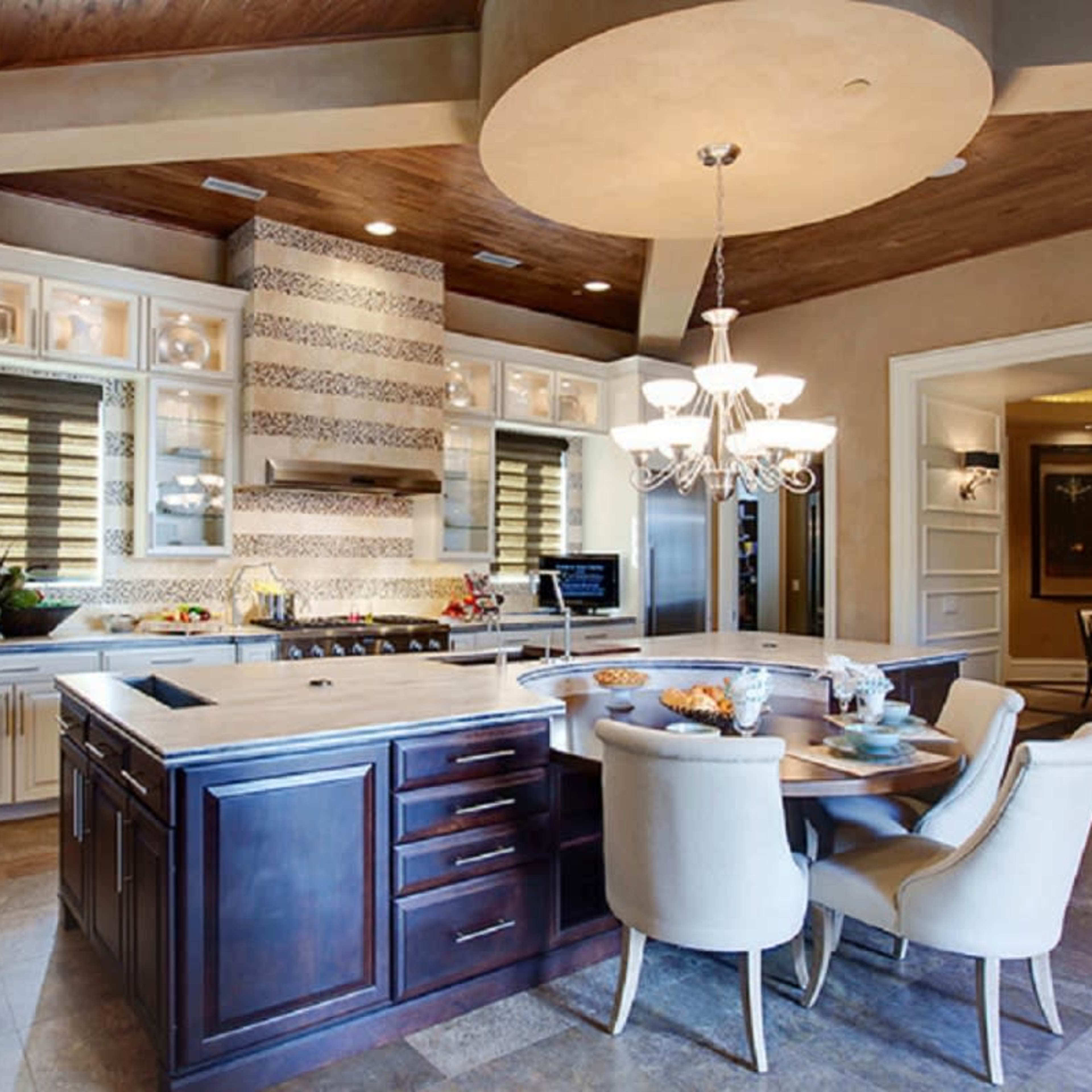 A modern kitchen with a central island, cabinetry, and a dining table set beneath a chandelier.