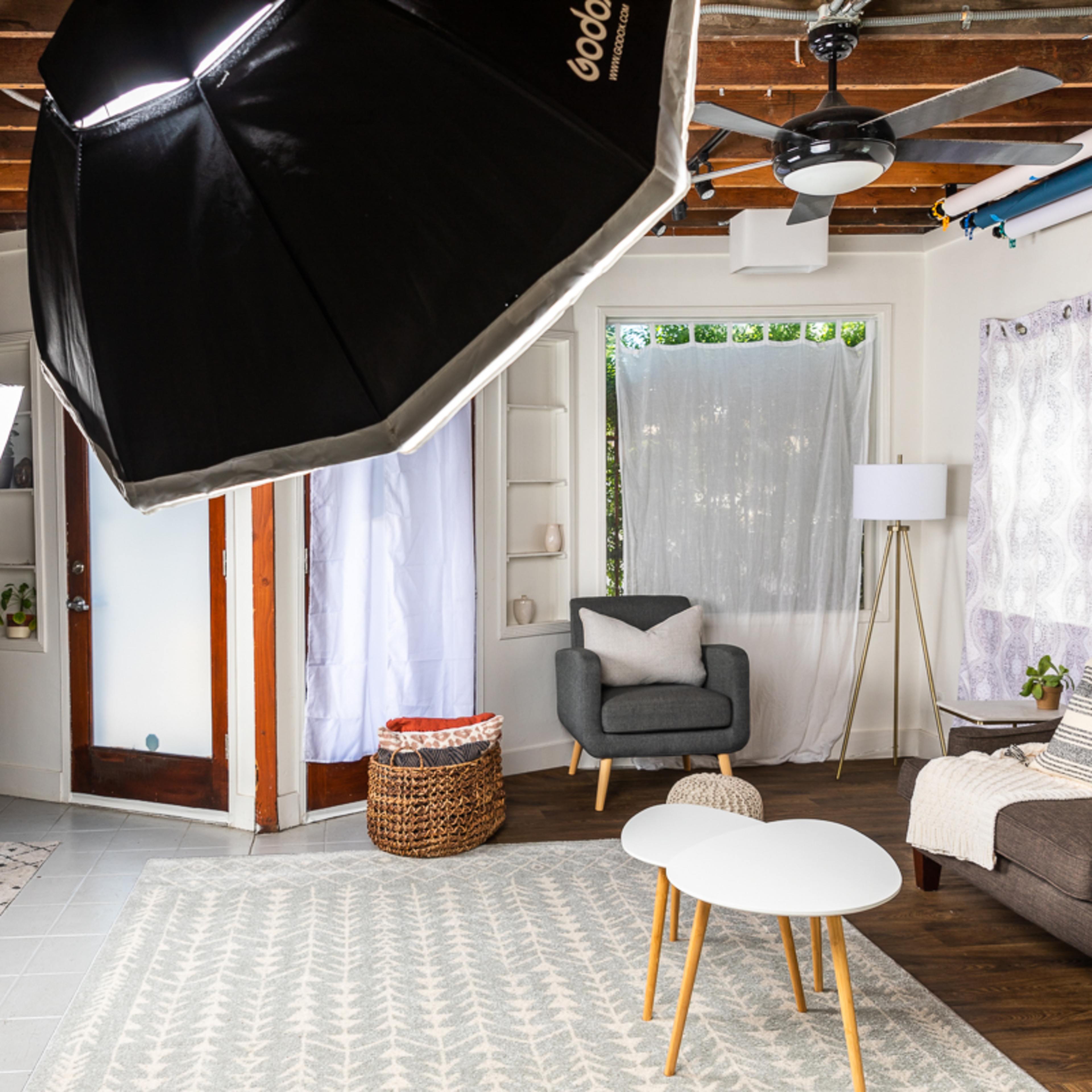 A well-lit living room setup with a gray sofa, a coffee table, and professional lighting equipment positioned around the space.