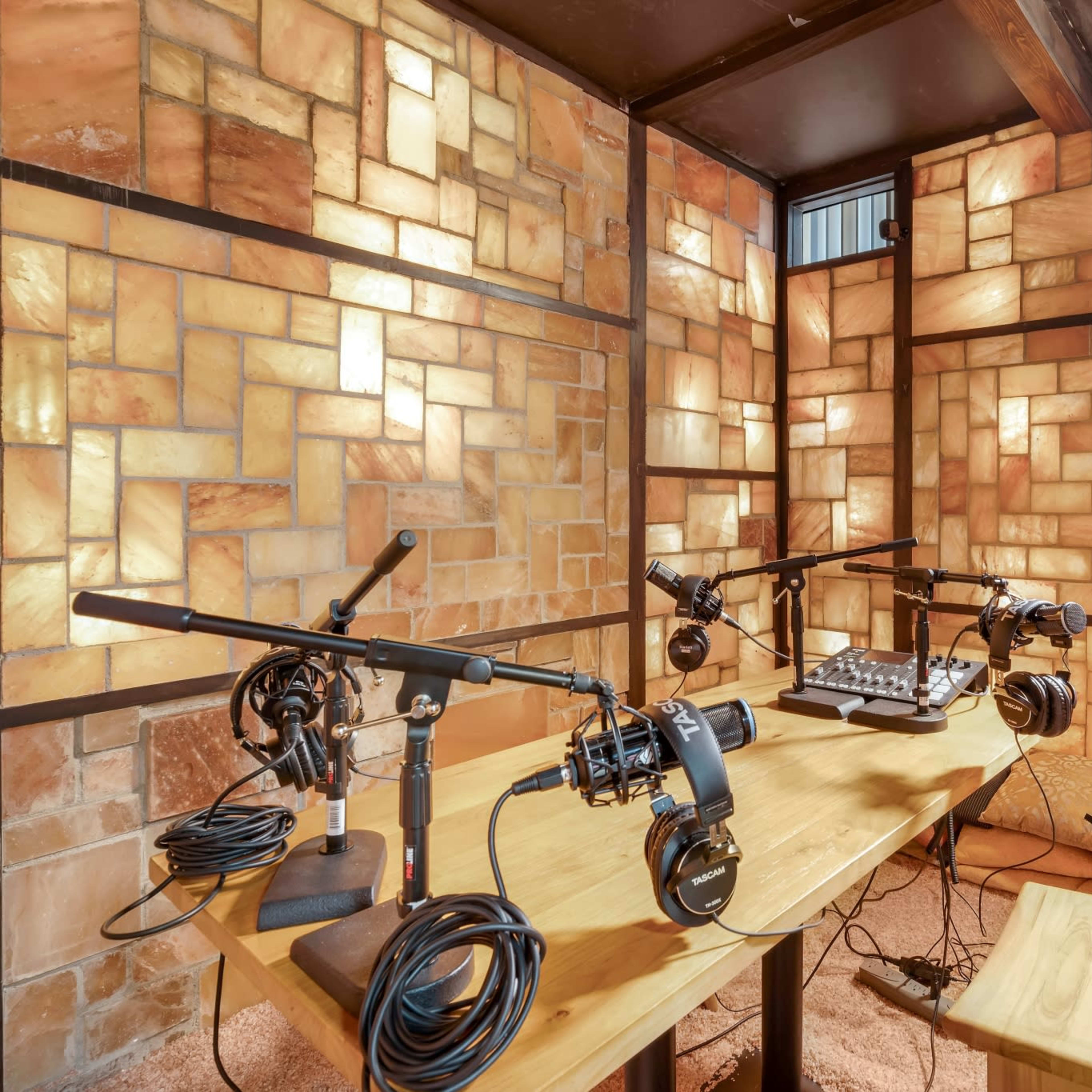 A recording studio featuring a wooden table with microphones, headphones, and audio equipment, surrounded by illuminated salt block walls.