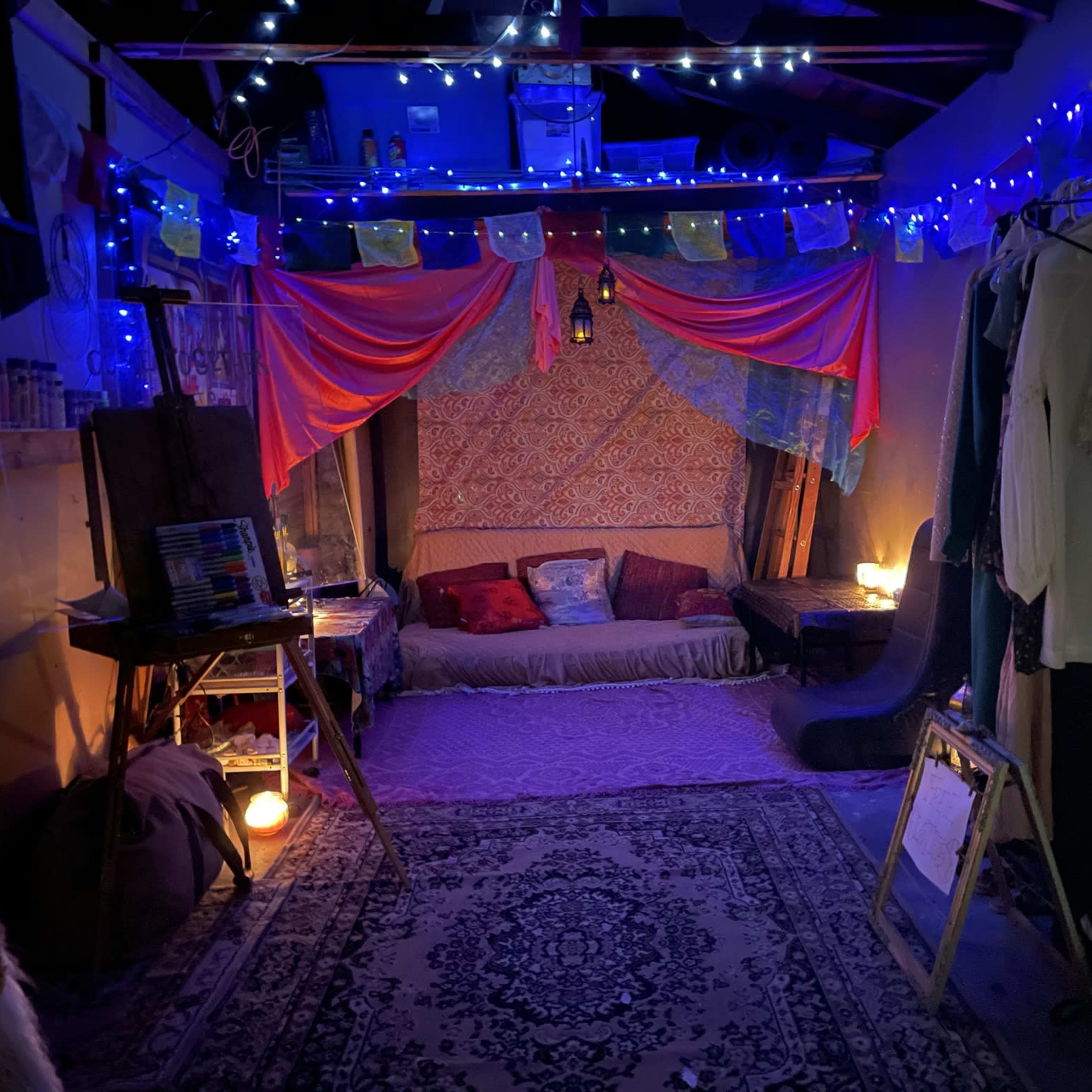 A cozy gathering space with colorful drapes, soft seating, and ambient lighting created by candles and string lights.
