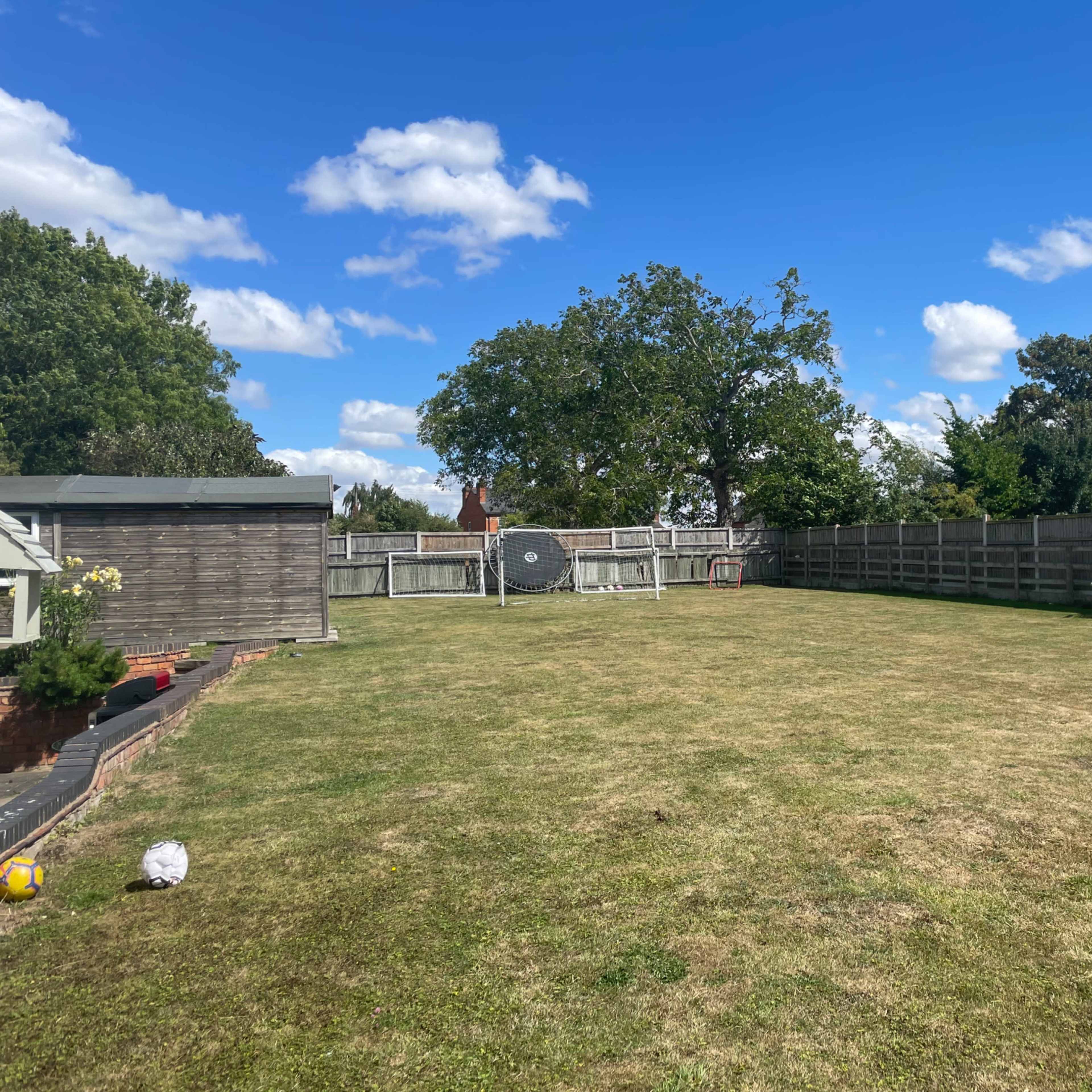 A large, open backyard with a grassy area, a fence surrounding it, and a few scattered objects.