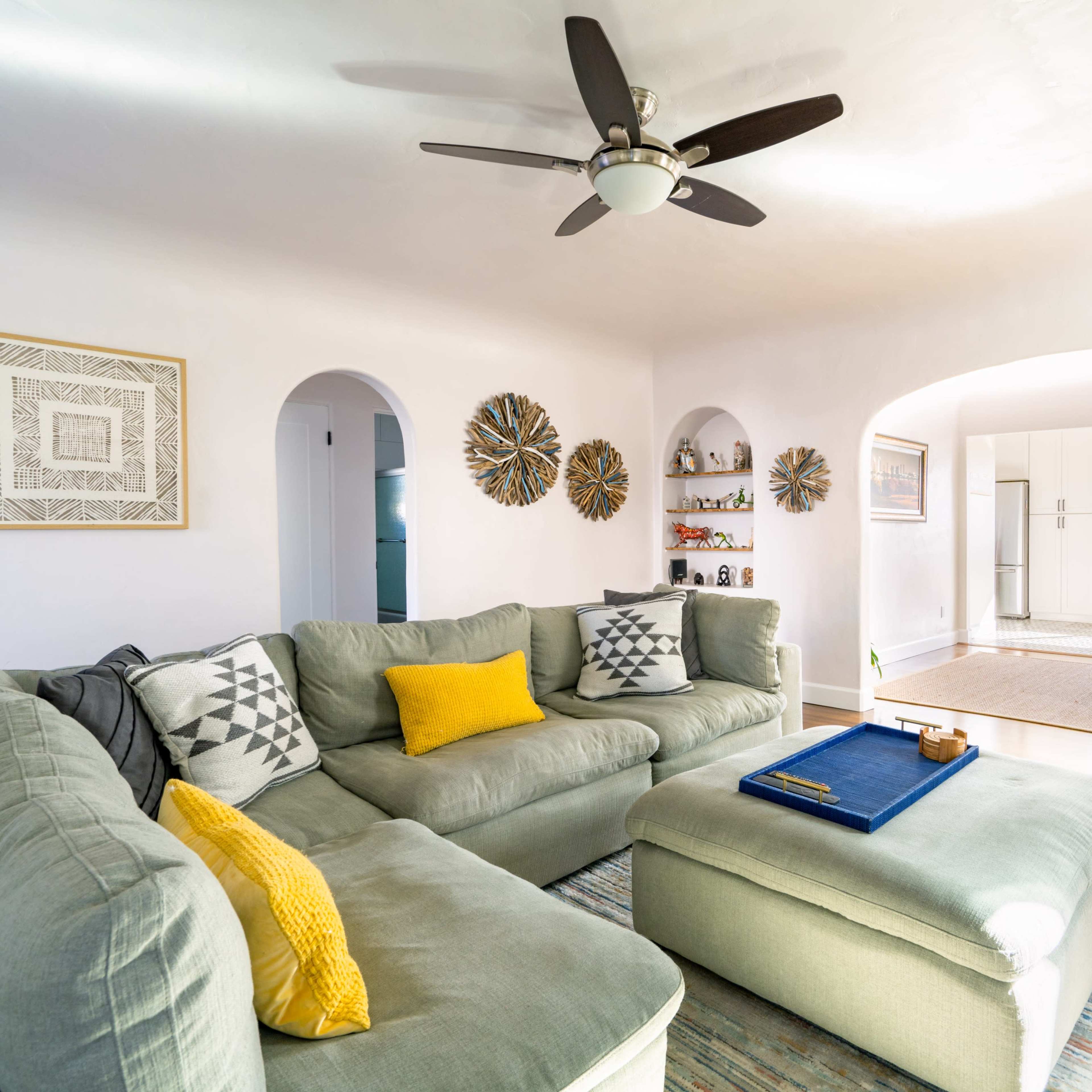 A spacious living room features a large, light green sectional sofa, a coffee table, and an open archway leading to a dining area.