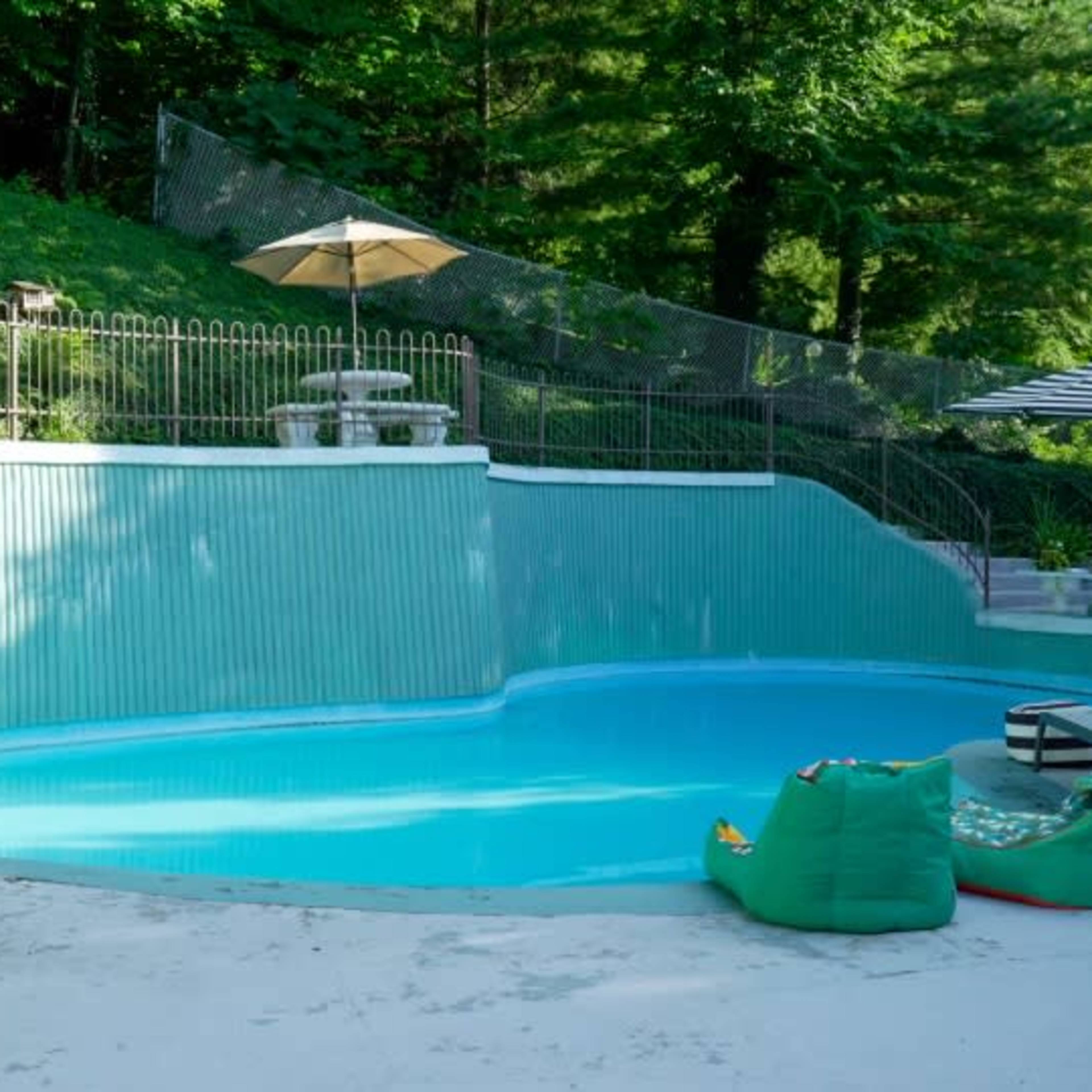 An empty swimming pool surrounded by a fence, with a lawn and seating area nearby.