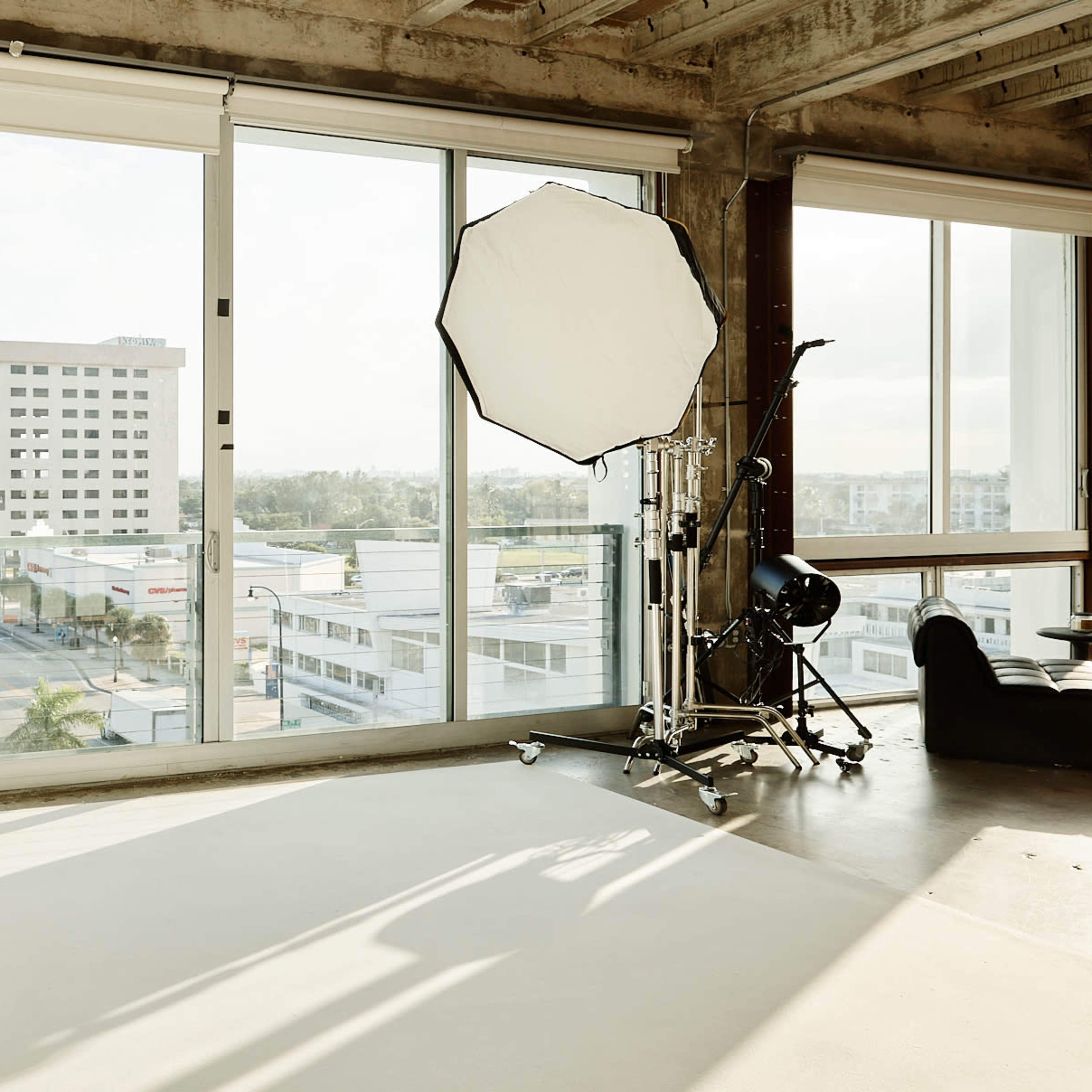 A spacious studio with large windows overlooking a cityscape, featuring a photography setup in one corner.