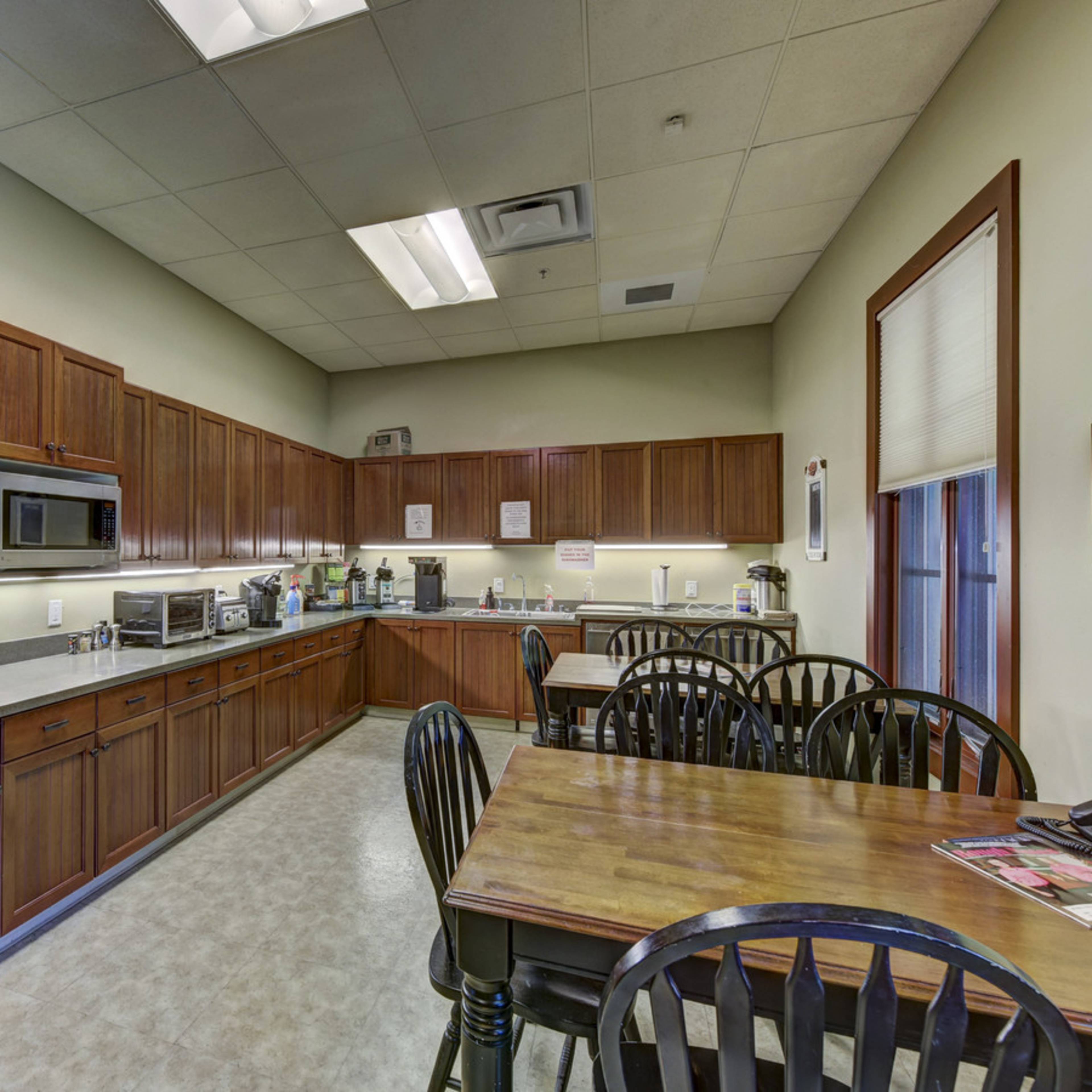A kitchen with wooden cabinets, a countertop, various kitchen appliances, and a dining table with black chairs.