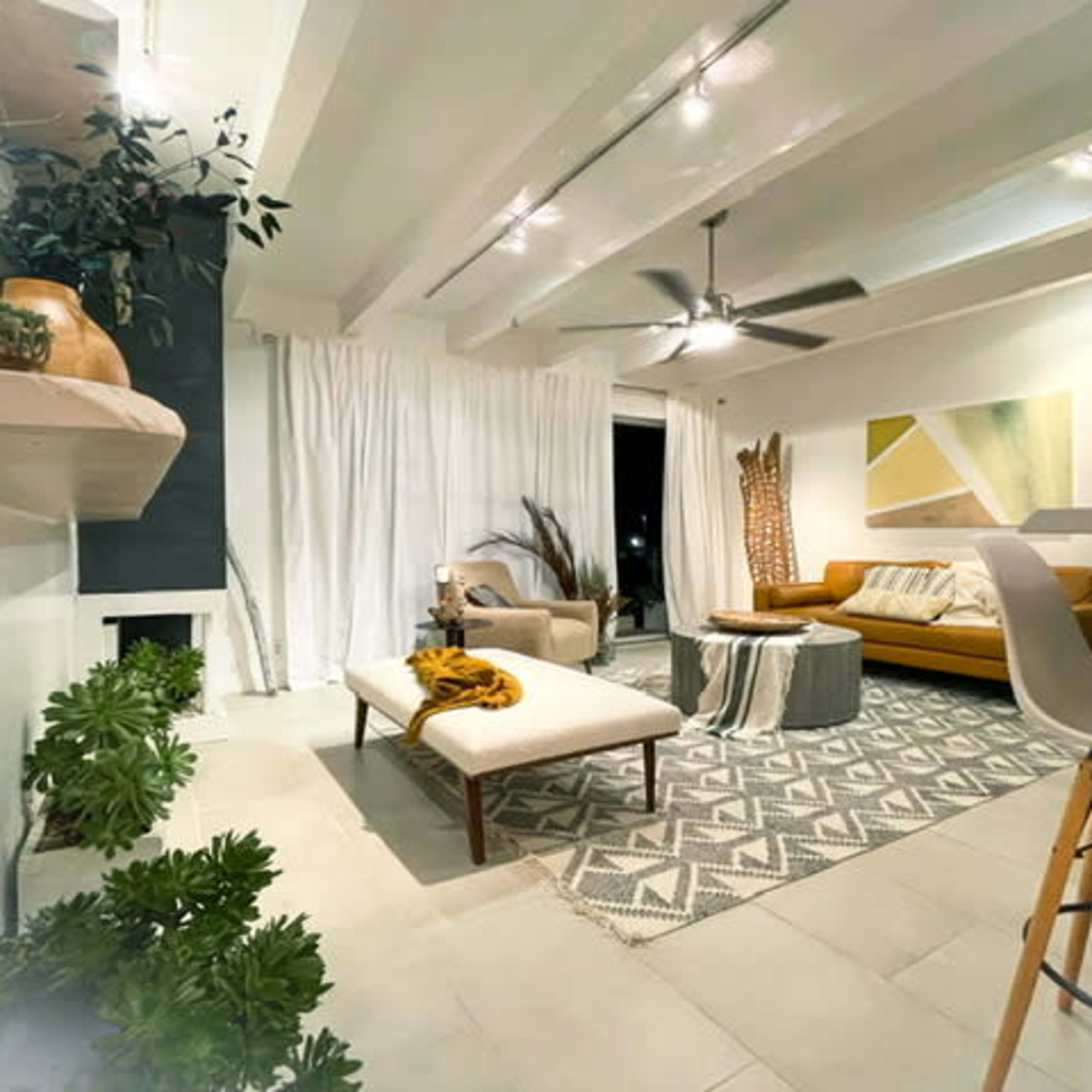 A modern living room with a couch, coffee table, patterned rug, and decorative plants, illuminated by ceiling lights.