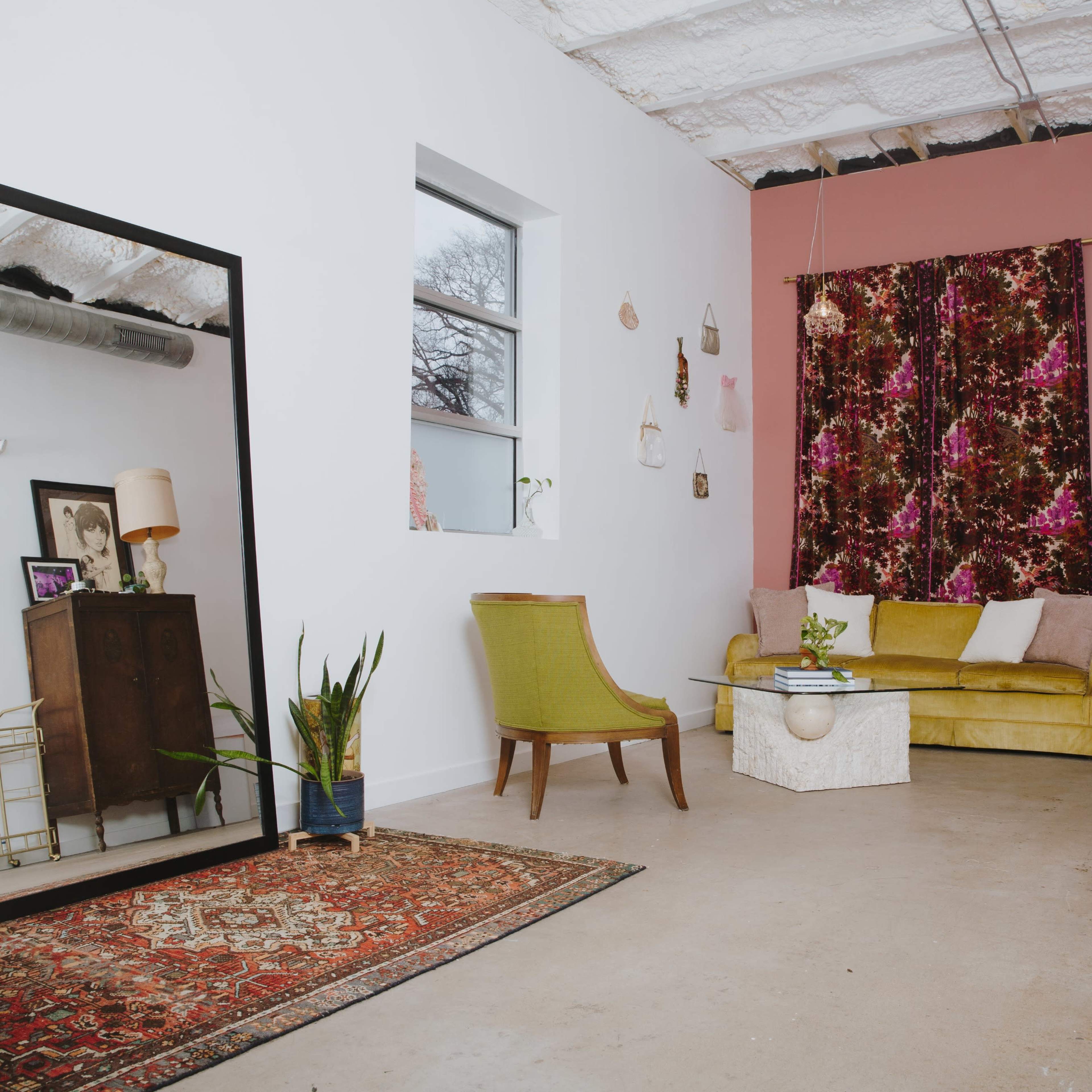 A modern living room featuring a yellow sofa, a mirror, a decorative rug, and a dark wooden cabinet against a painted wall.