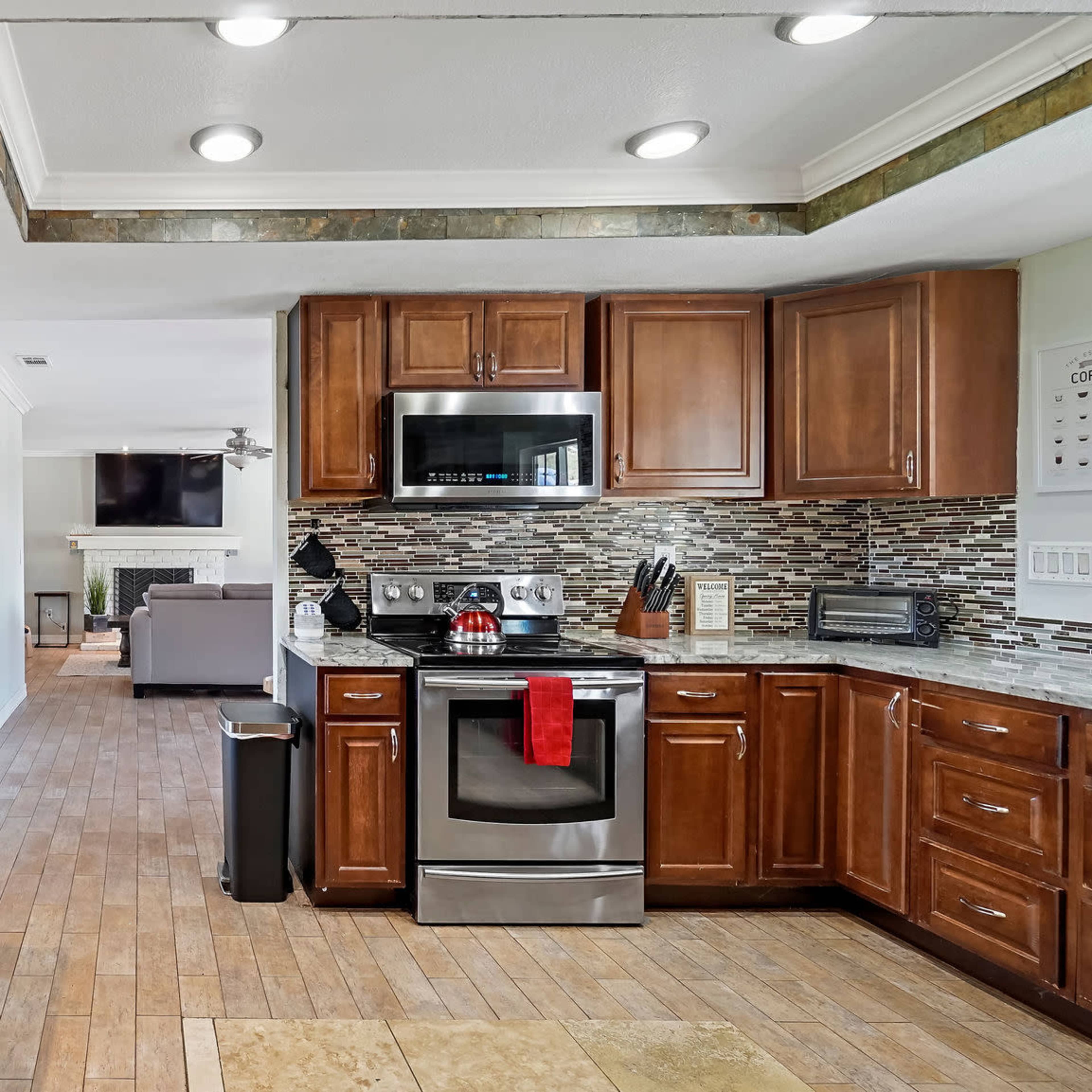 The kitchen features wooden cabinets, granite countertops, and modern stainless steel appliances, with an open layout that connects to a living area.