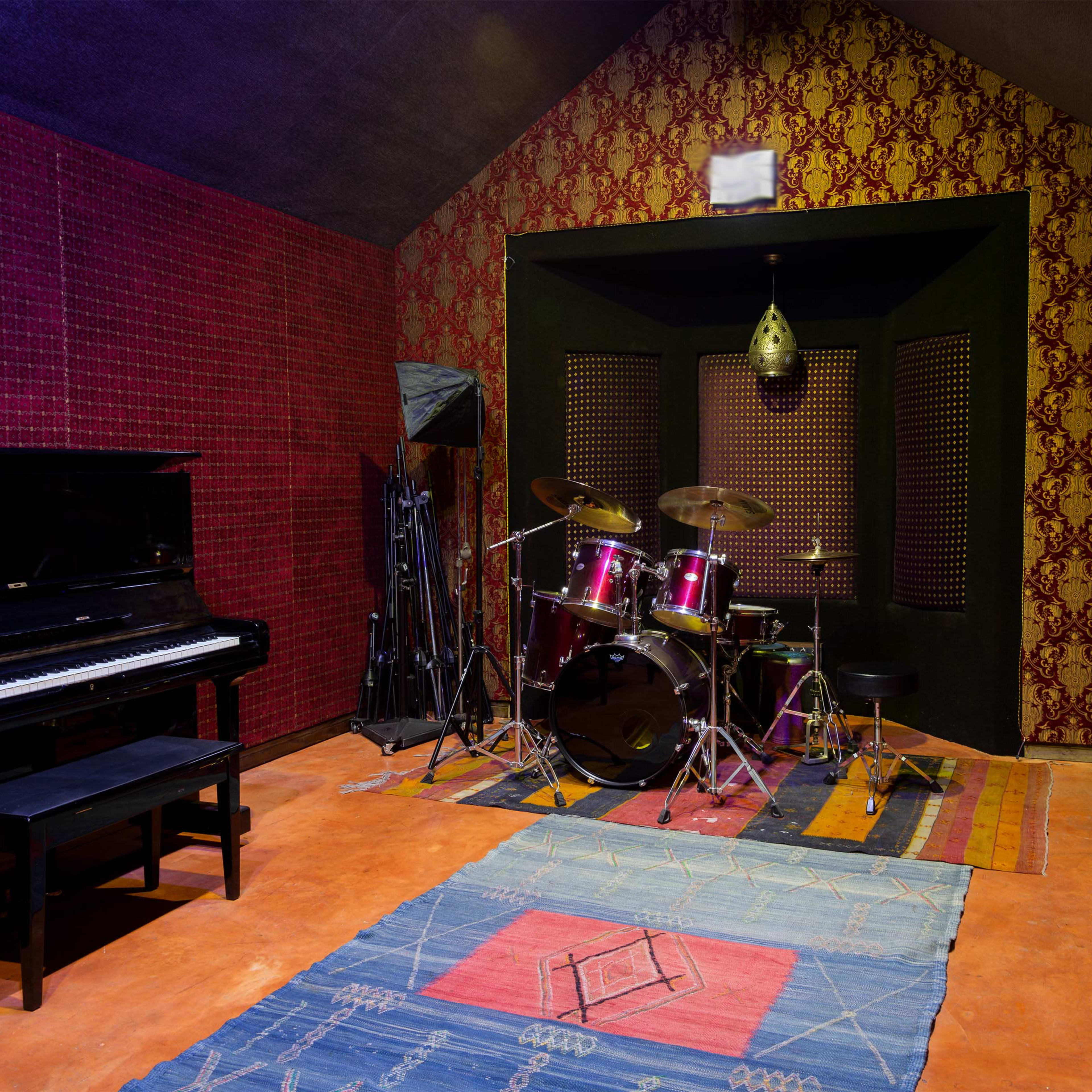 A music studio featuring a grand piano on one side and a drum set on the other, surrounded by red patterned walls.