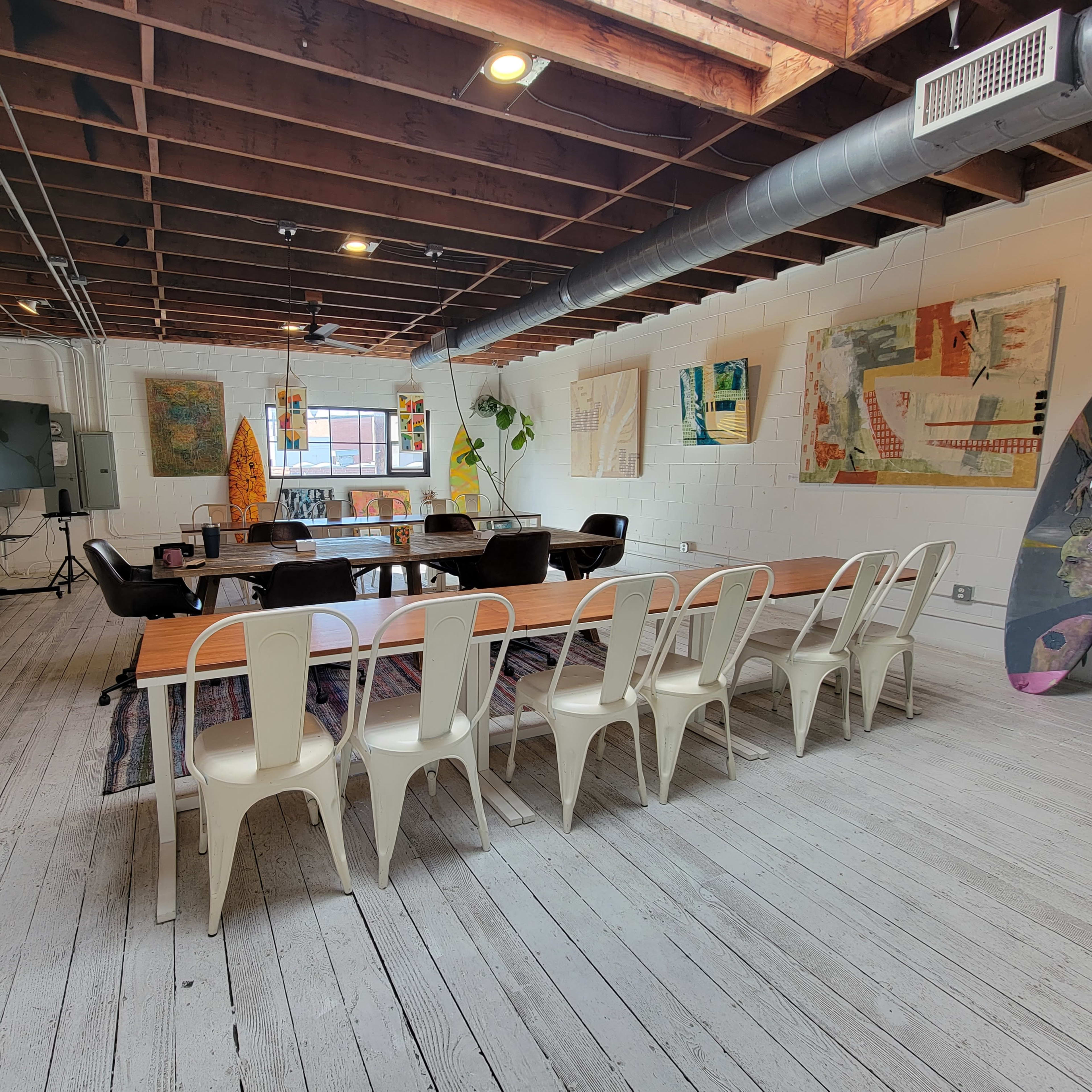 A spacious meeting room features a long wooden table with chairs, a large screen, and artwork displayed on the walls.