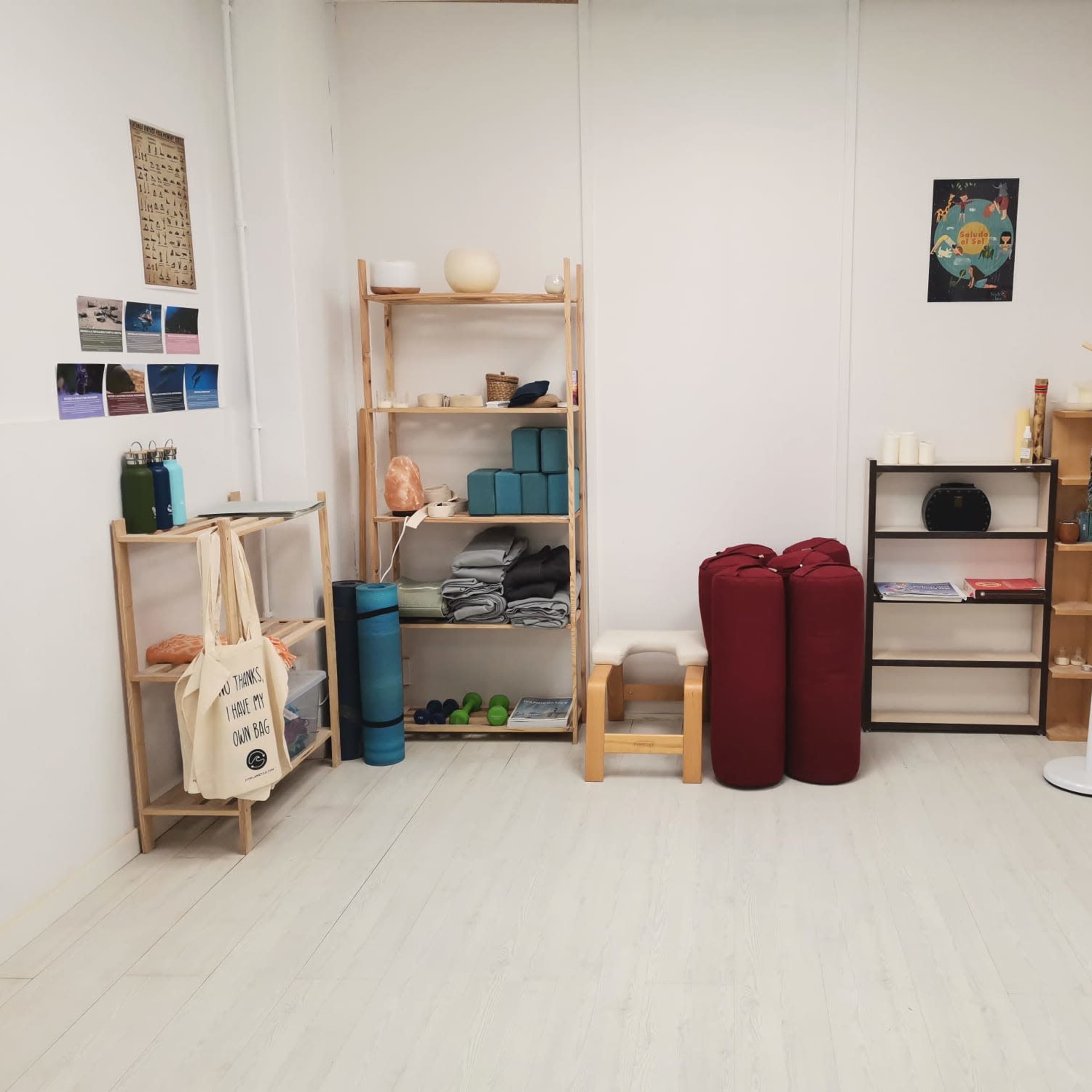 A minimalist room with wooden shelving units, a coat stand, and various items like yoga mats, cushions, and decorative elements.