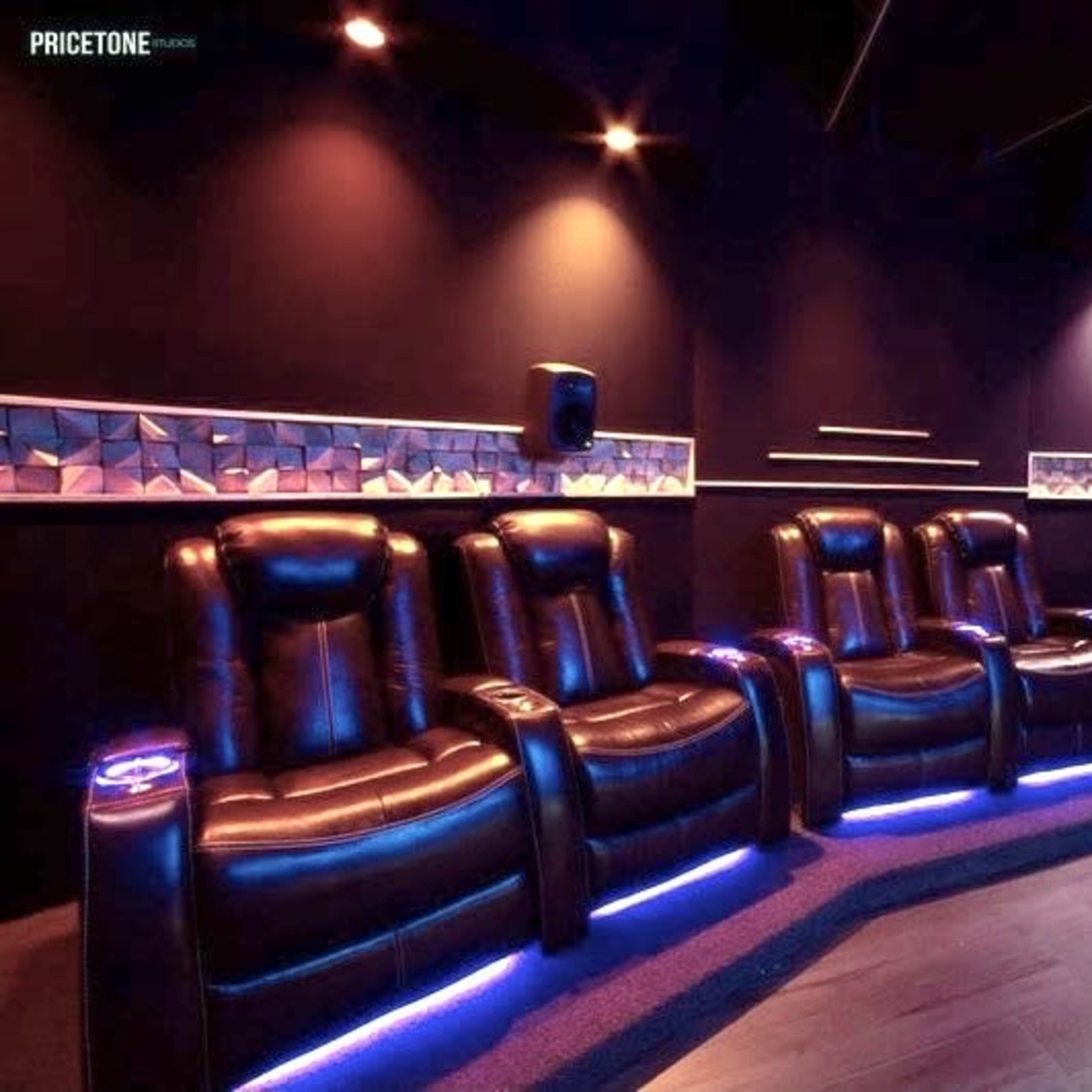 A dark home theater room featuring five black leather reclining chairs, illuminated by soft blue lighting.