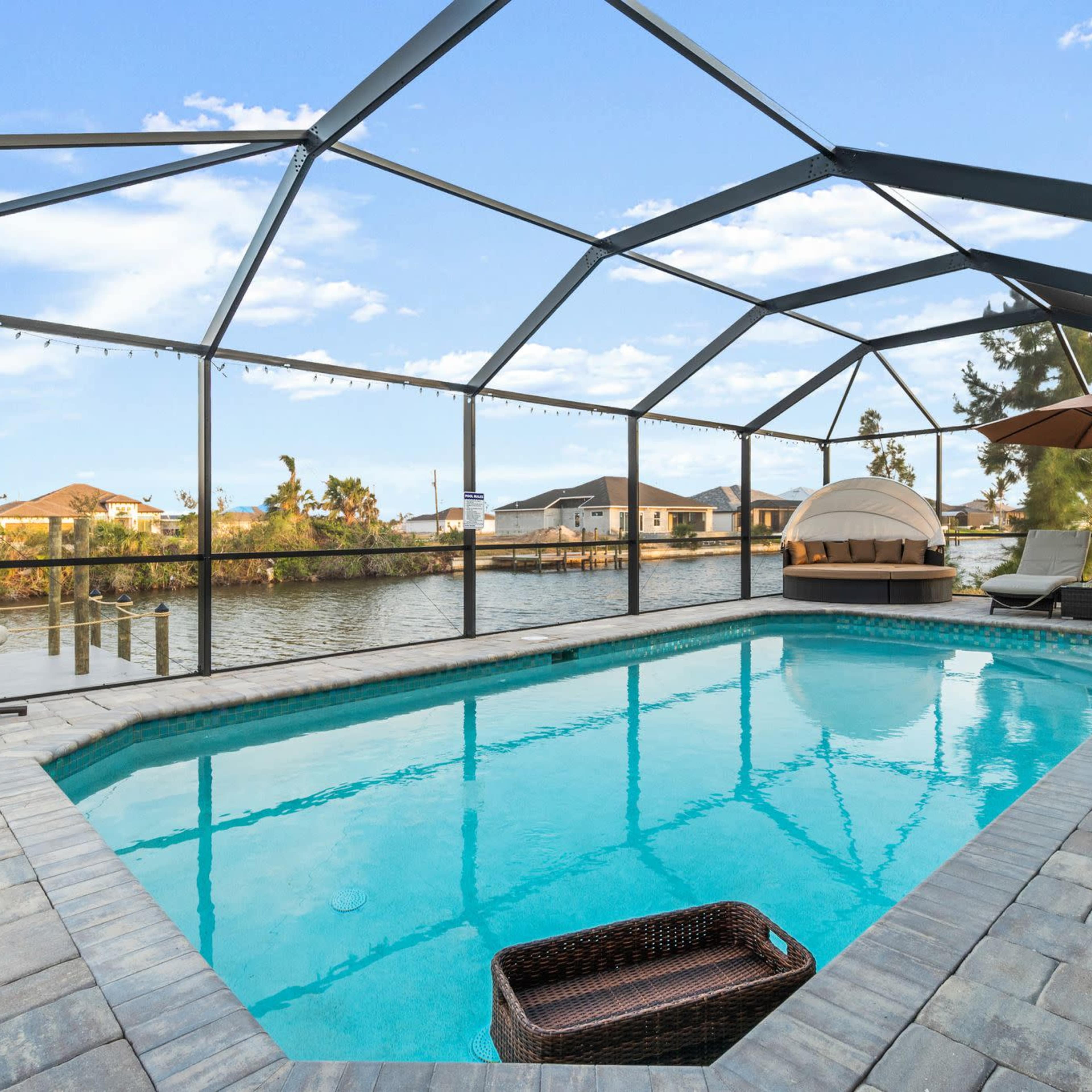 A screened-in swimming pool area with a view of a waterfront and several homes in the background.