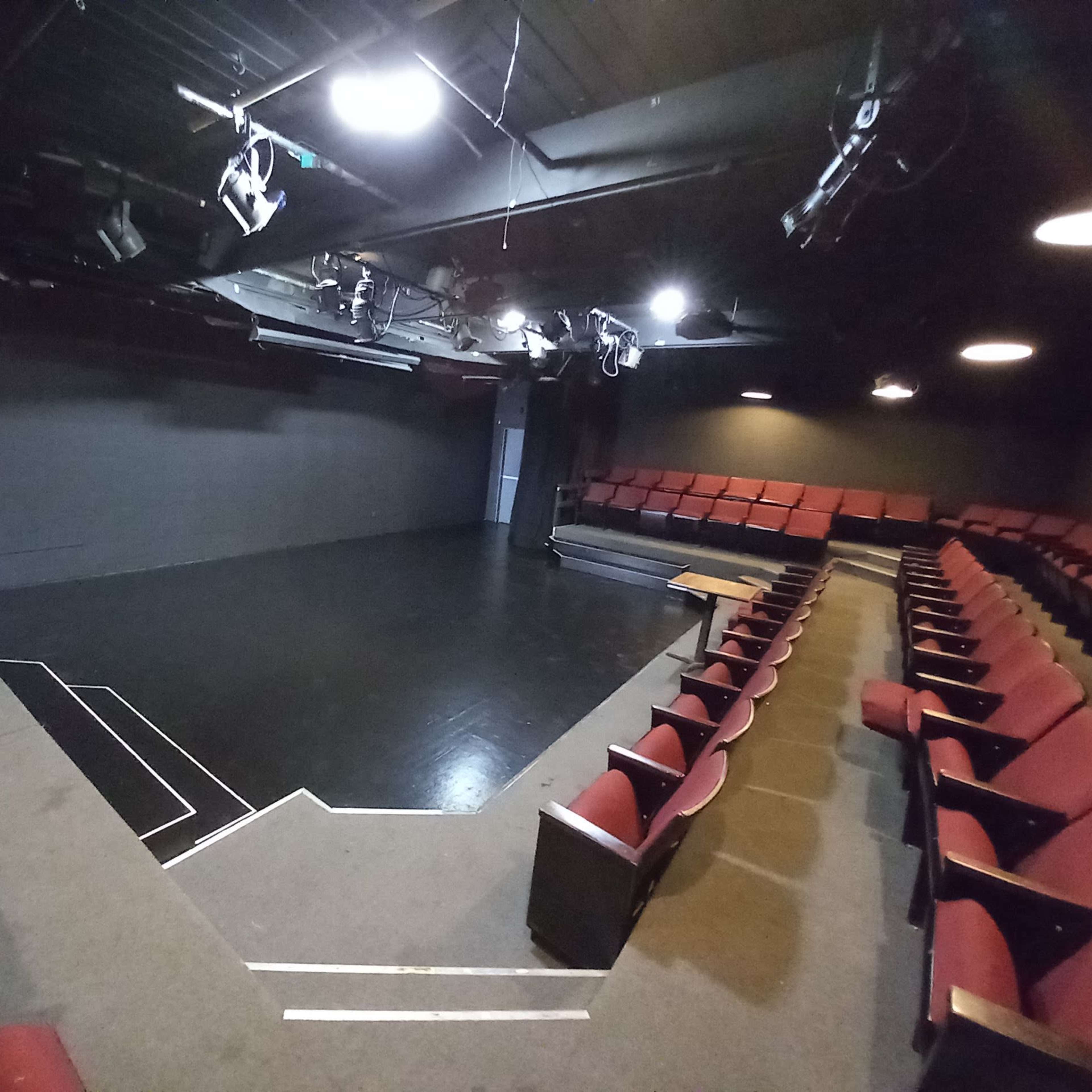 A small theater with red seating arranged in a semi-circular layout facing a polished black stage.
