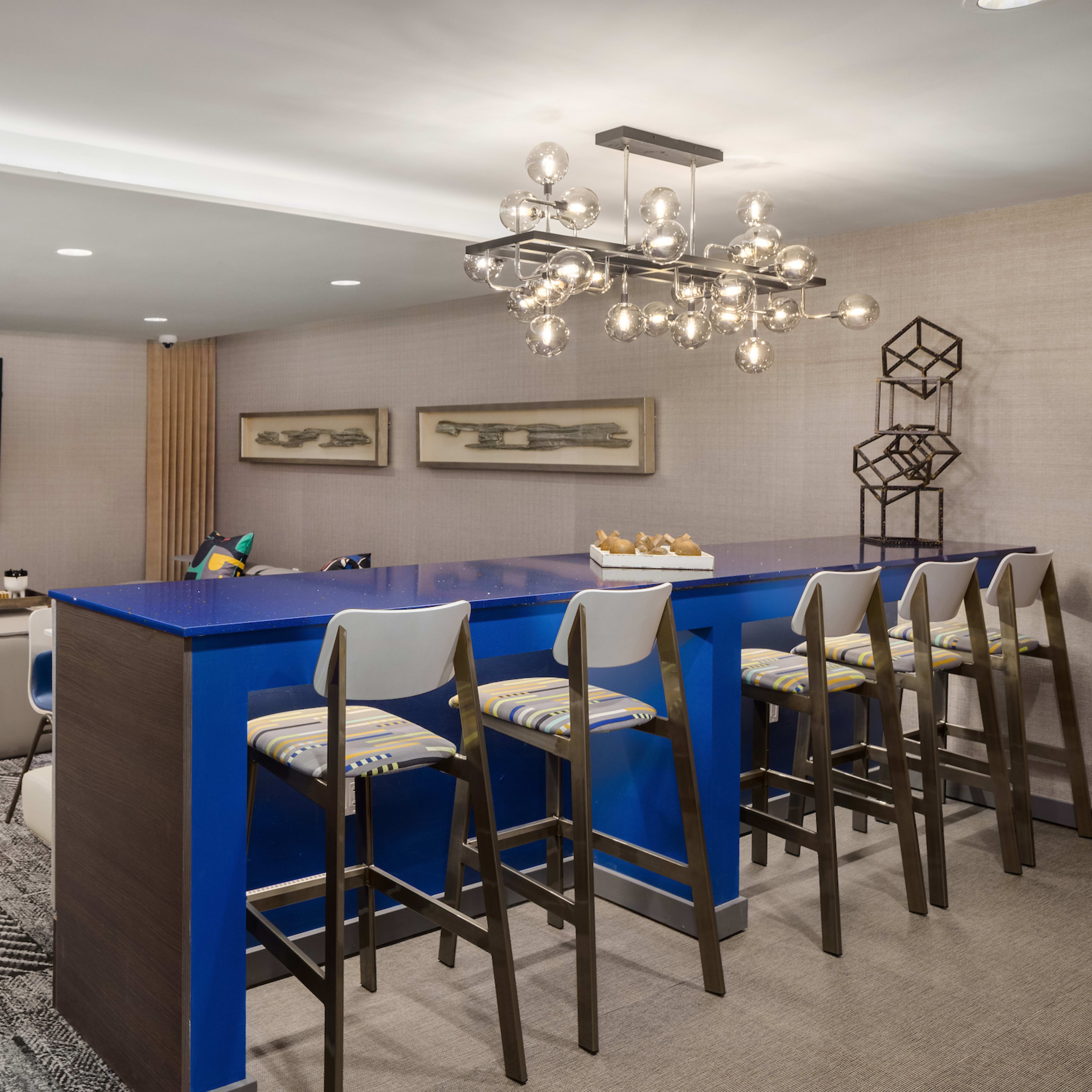 A modern lounge area featuring a blue counter bar with high stools, a large flat-screen TV on the wall, and contemporary artwork.