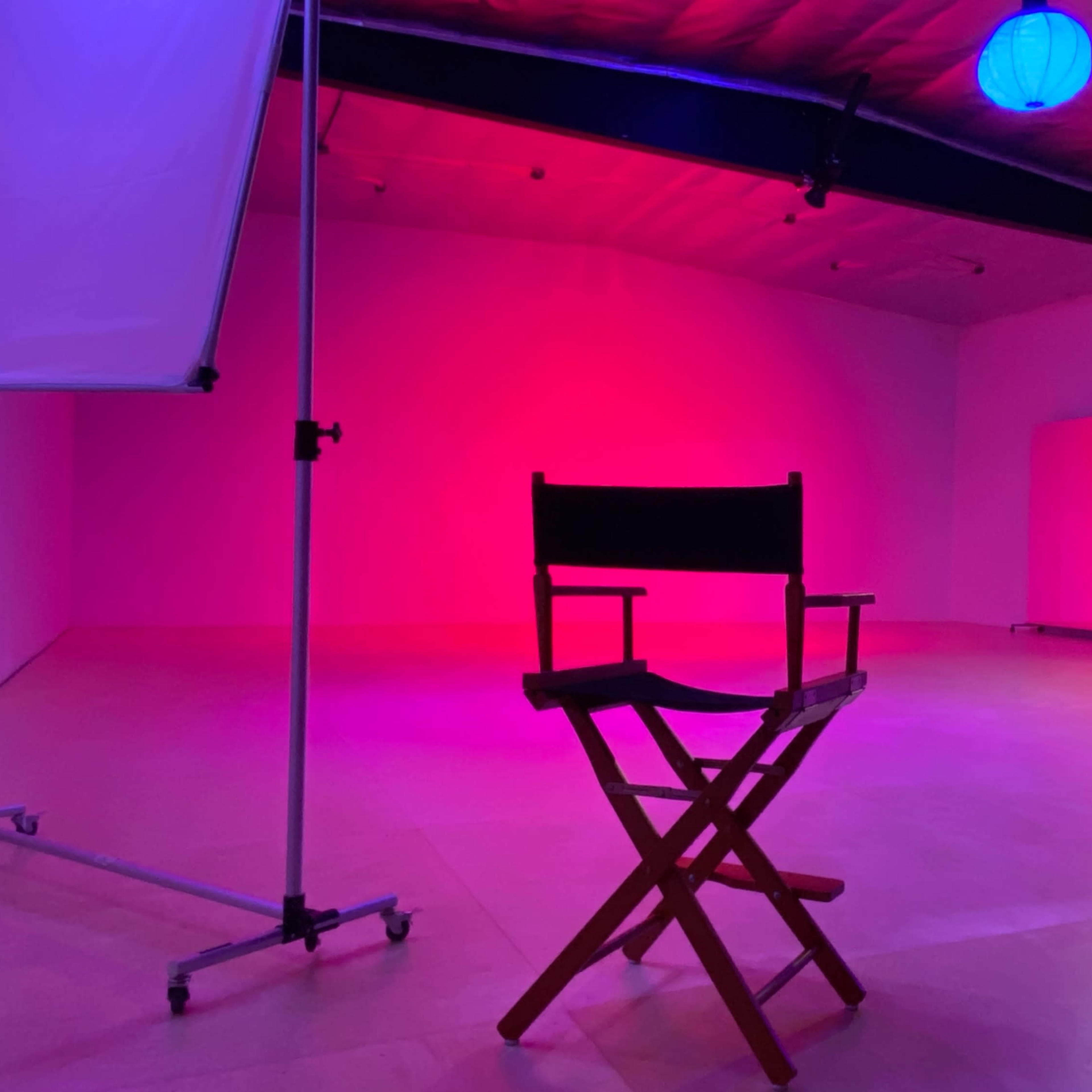 An empty studio space featuring a director's chair, colored lighting, and a large mirror.