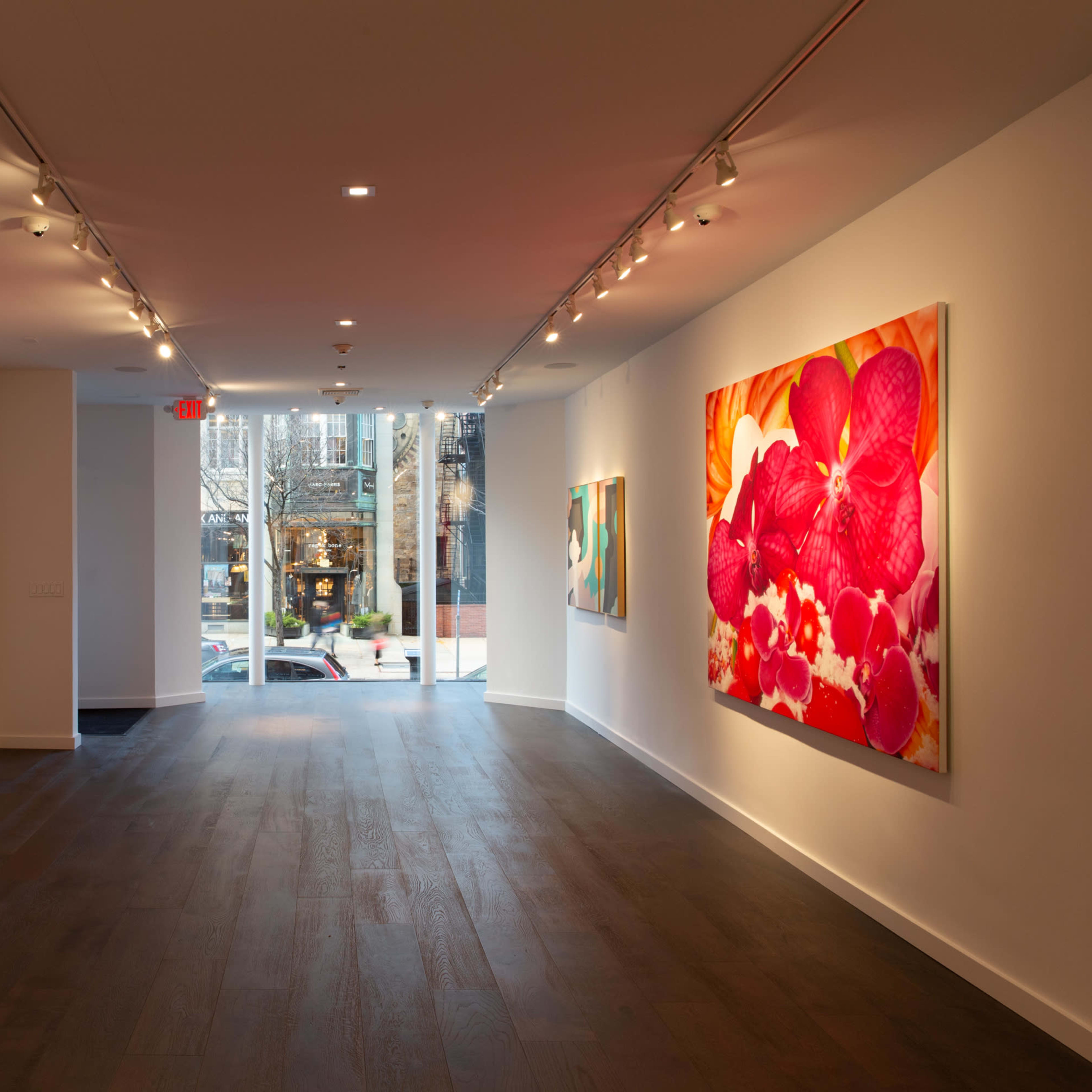 An art gallery with large floral paintings on two walls and a view of the street through a glass entrance.