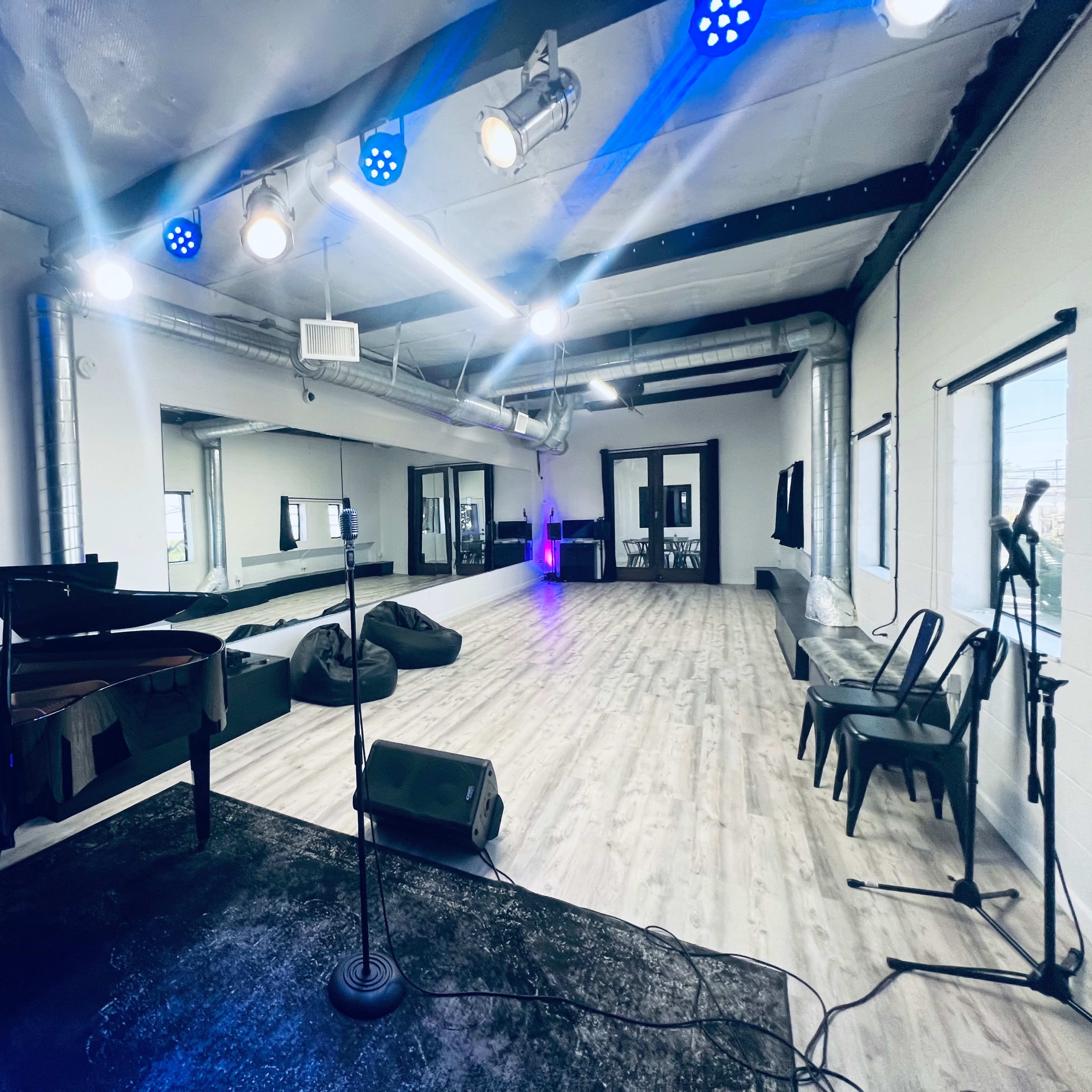 A spacious, well-lit room with a grand piano, microphone setup, and seating arranged for a performance.