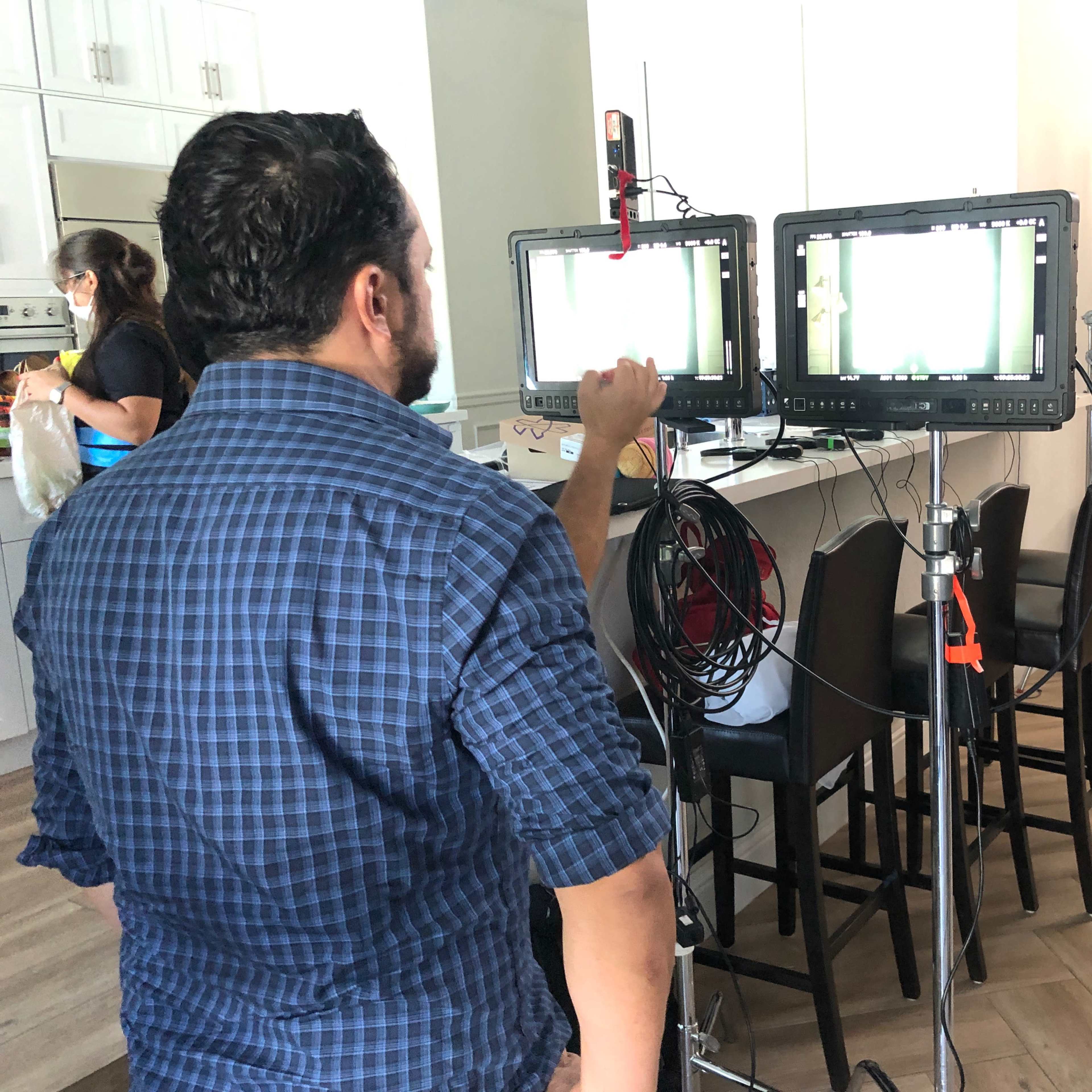 A man adjusts video monitors on a film set while crew members work in the background.