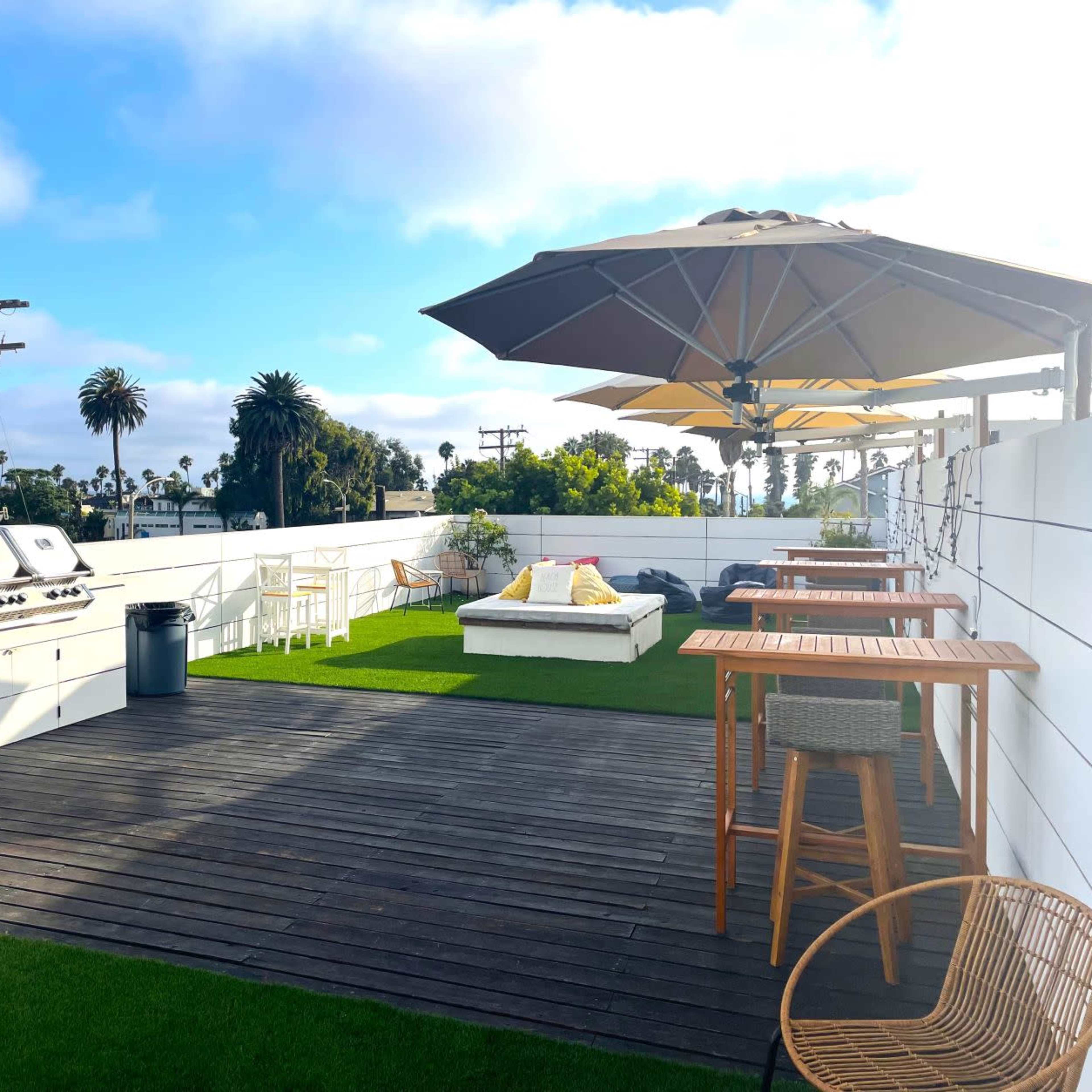 A rooftop terrace with a barbecue grill, seating areas under umbrellas, and artificial grass.