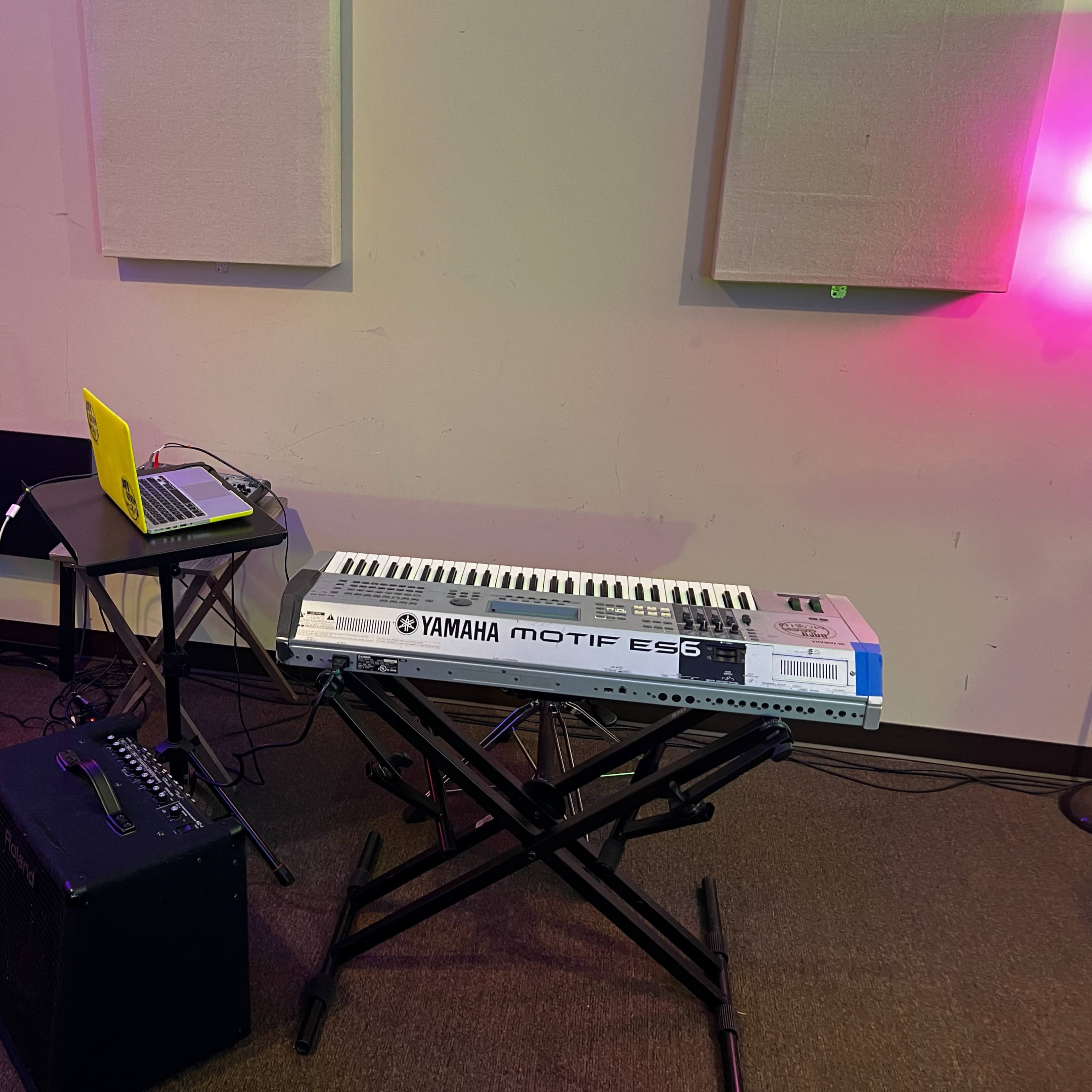 A Yamaha Motif ES6 keyboard is set up alongside a laptop and a sound mixer in a music studio with padded walls.