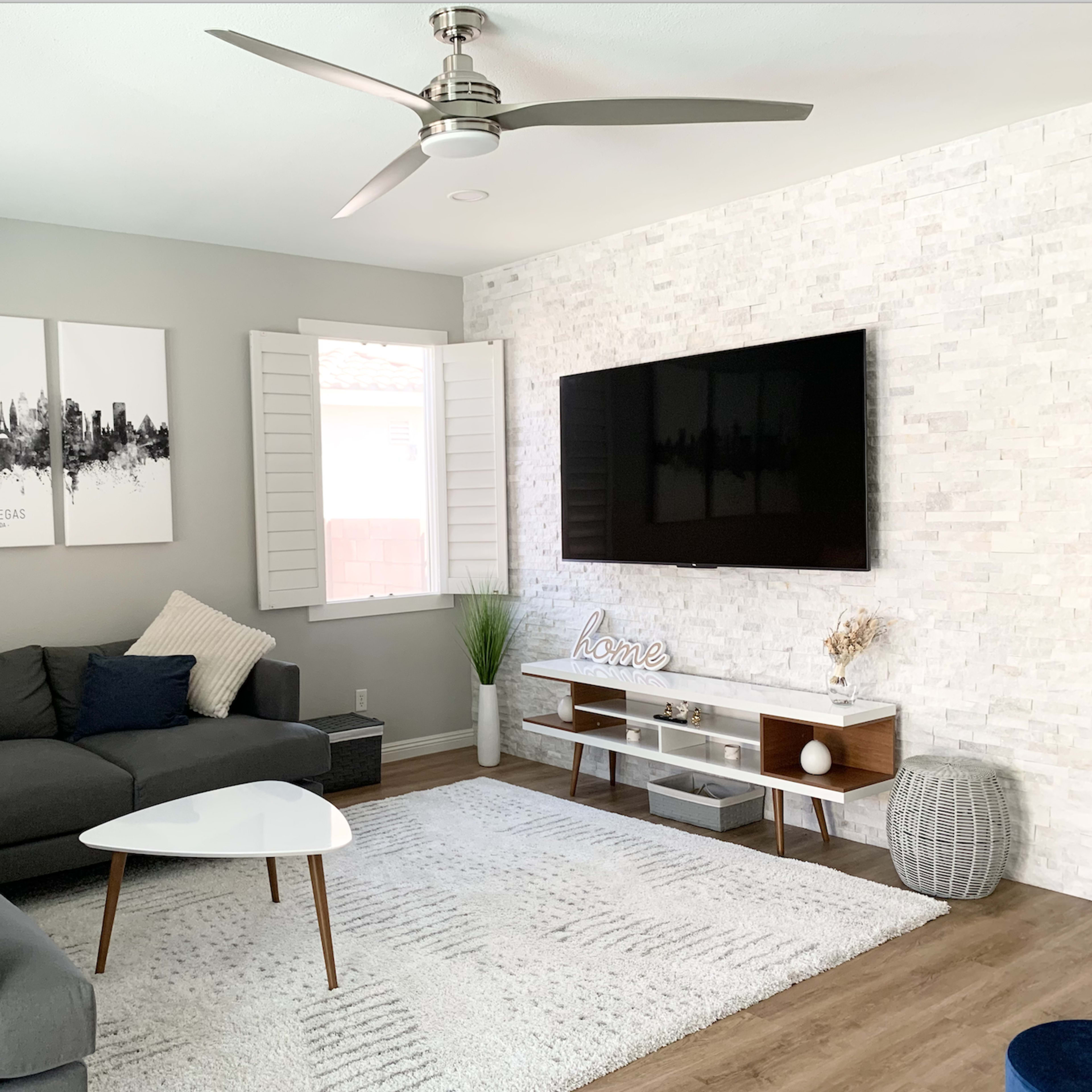 The living room features a gray sectional sofa, a wall-mounted television, and a decorative area with framed artwork and potted plants.