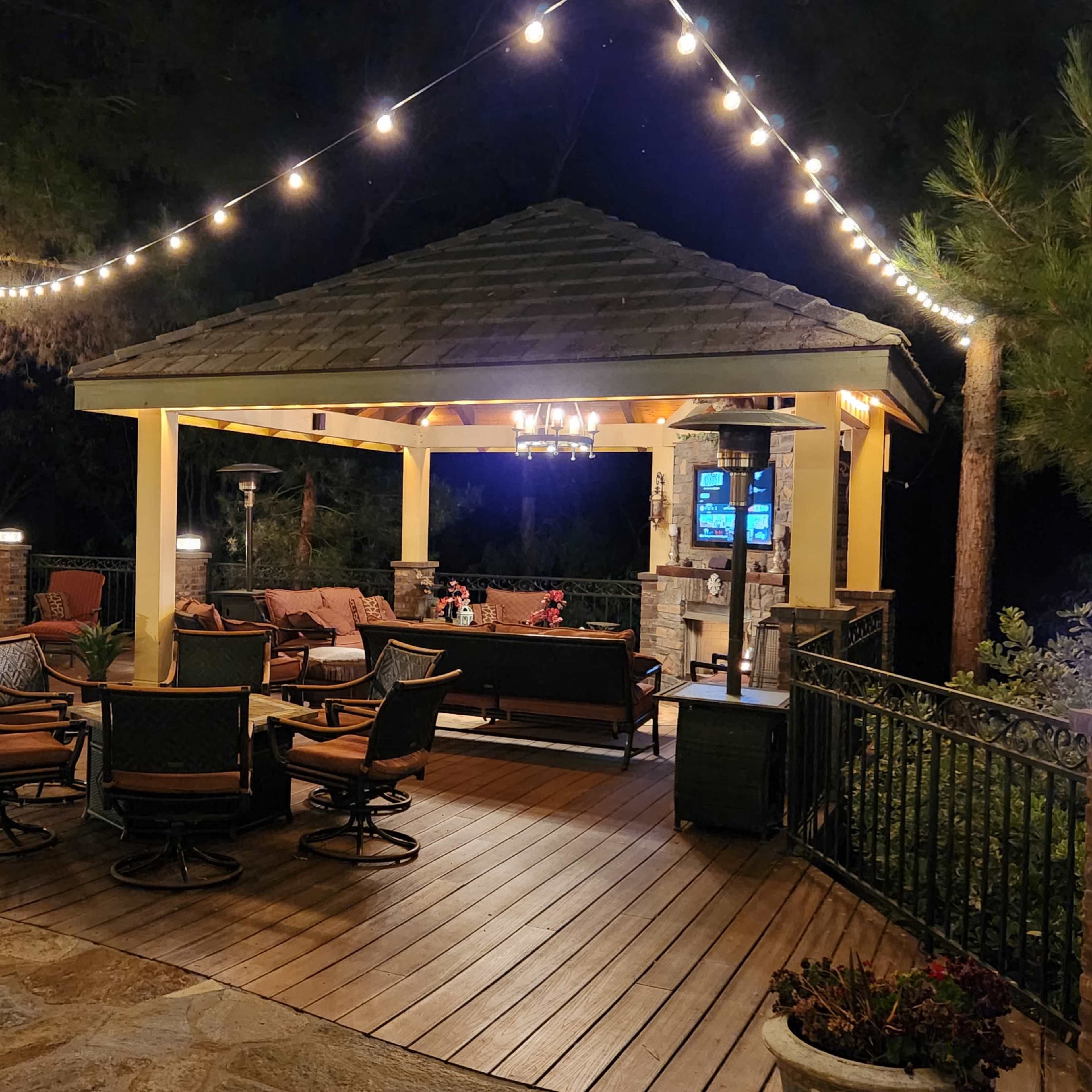 A well-lit outdoor patio area with a covered seating space, a grill station, and string lights overhead at night.
