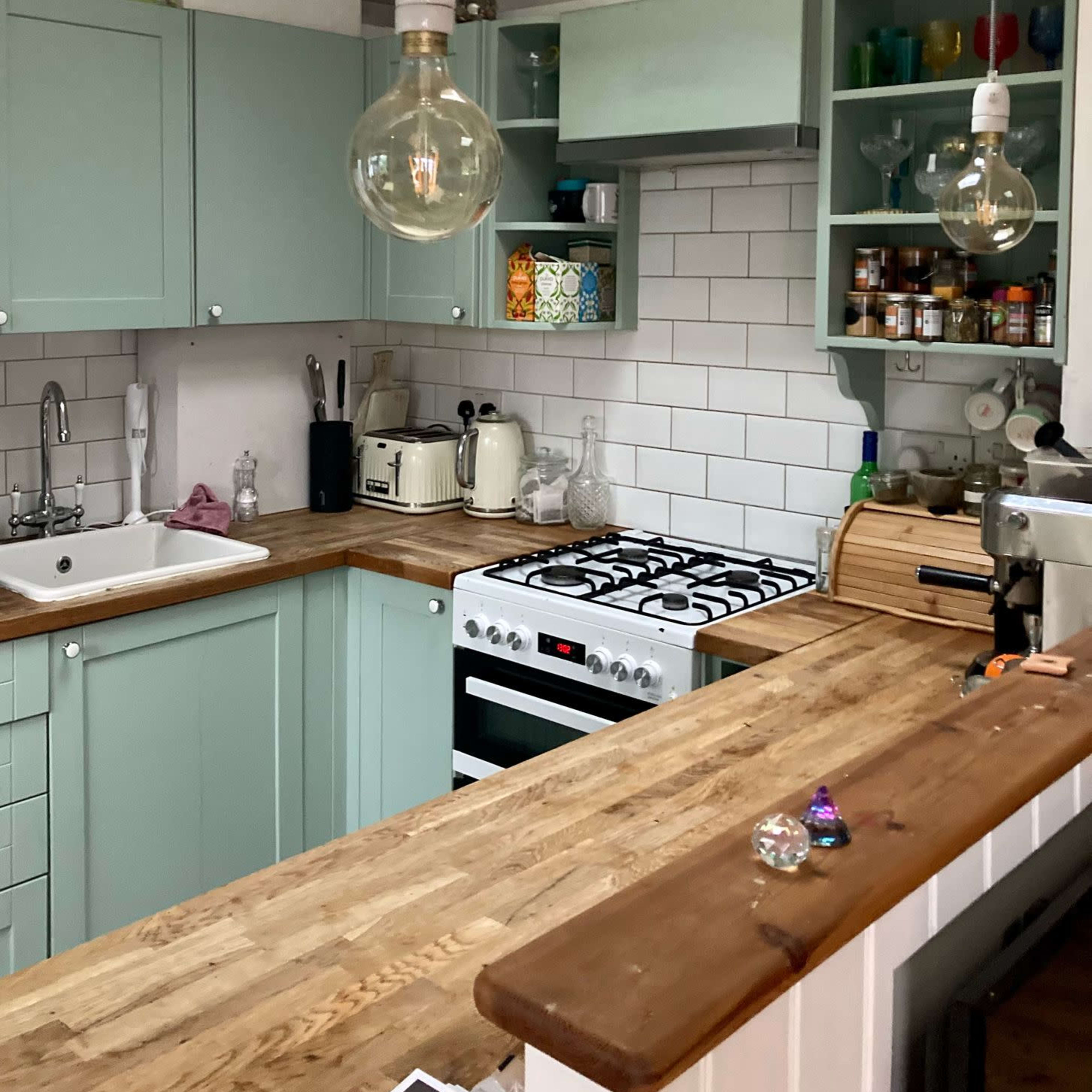 A modern kitchen features mint green cabinets, white subway tiles, a wooden countertop, and pendant lighting above the workspace.