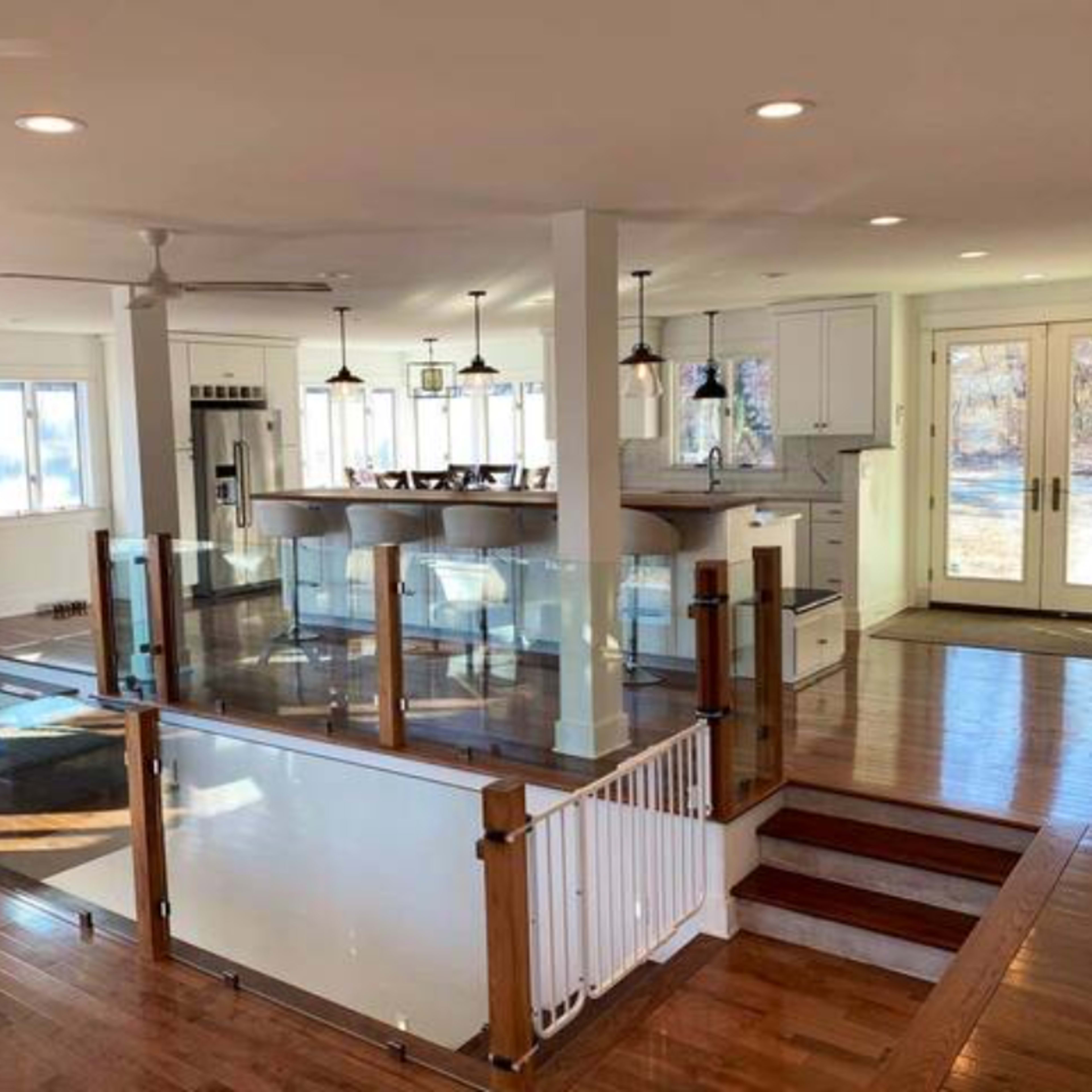 A spacious, modern interior with a kitchen area visible from an open living space, featuring hardwood floors and large windows.